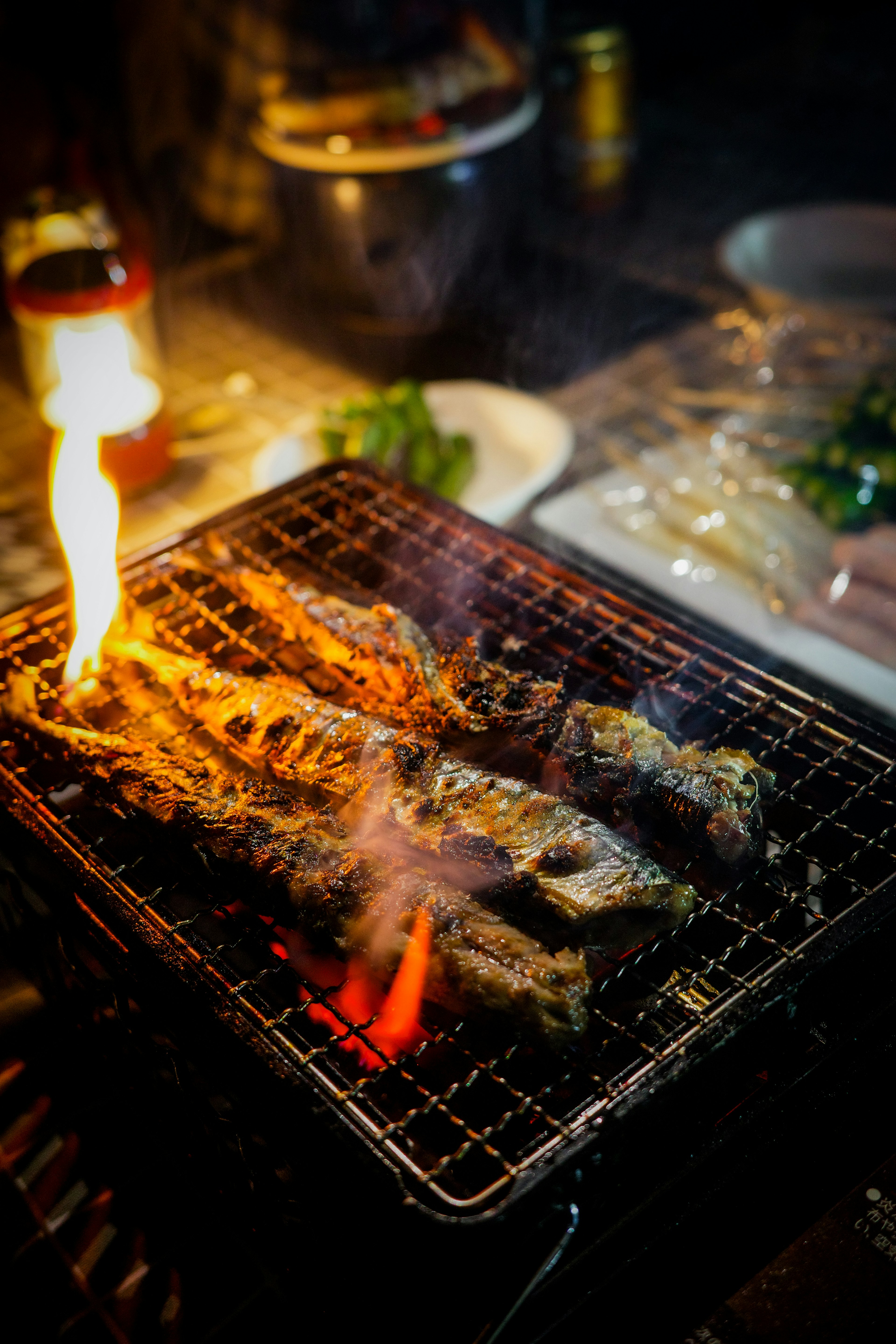 炭火で焼かれた魚の串焼きが炎を上げている