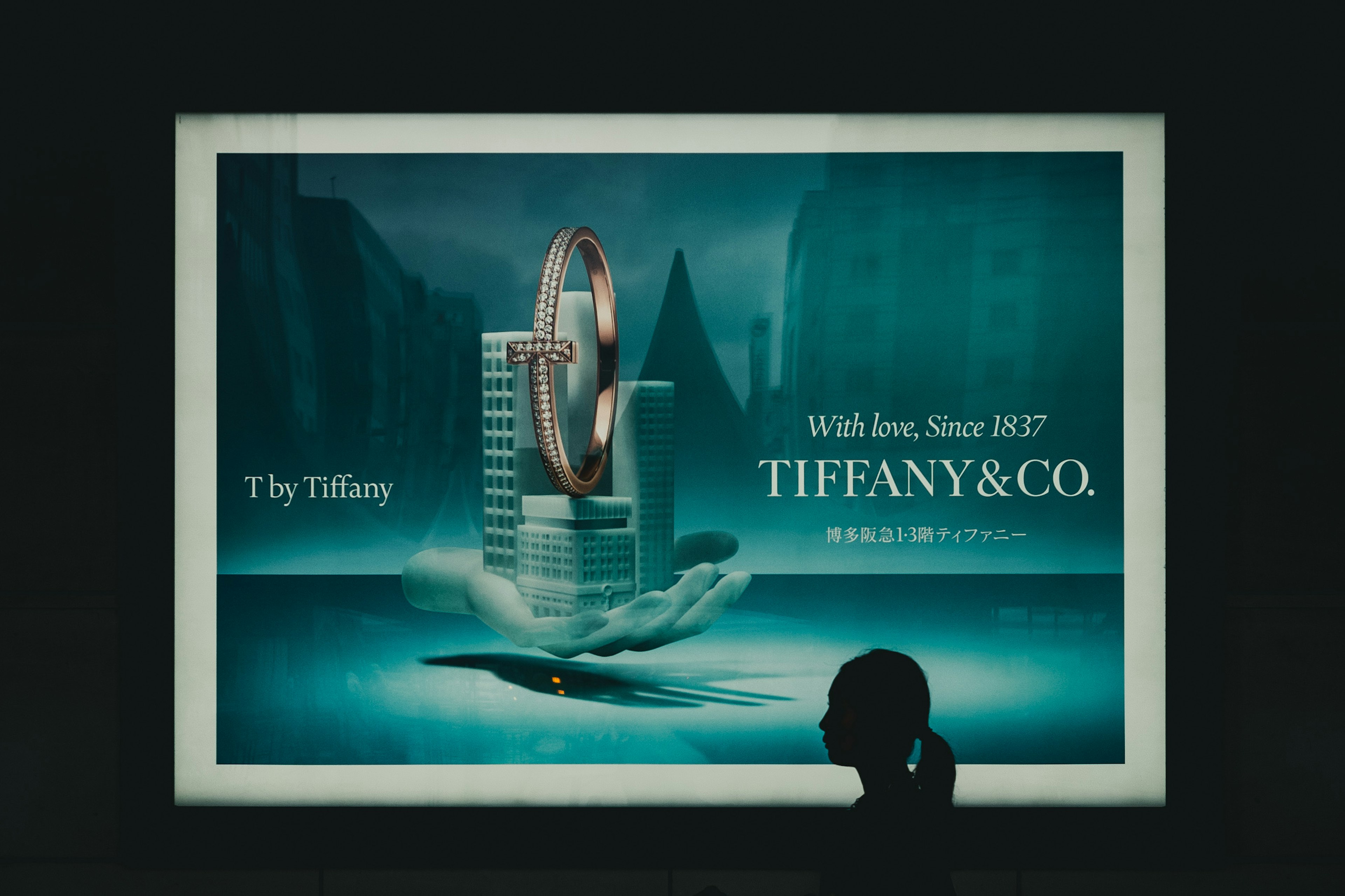 Publicidad de Tiffany que presenta un anillo sostenido por una mano con un fondo urbano