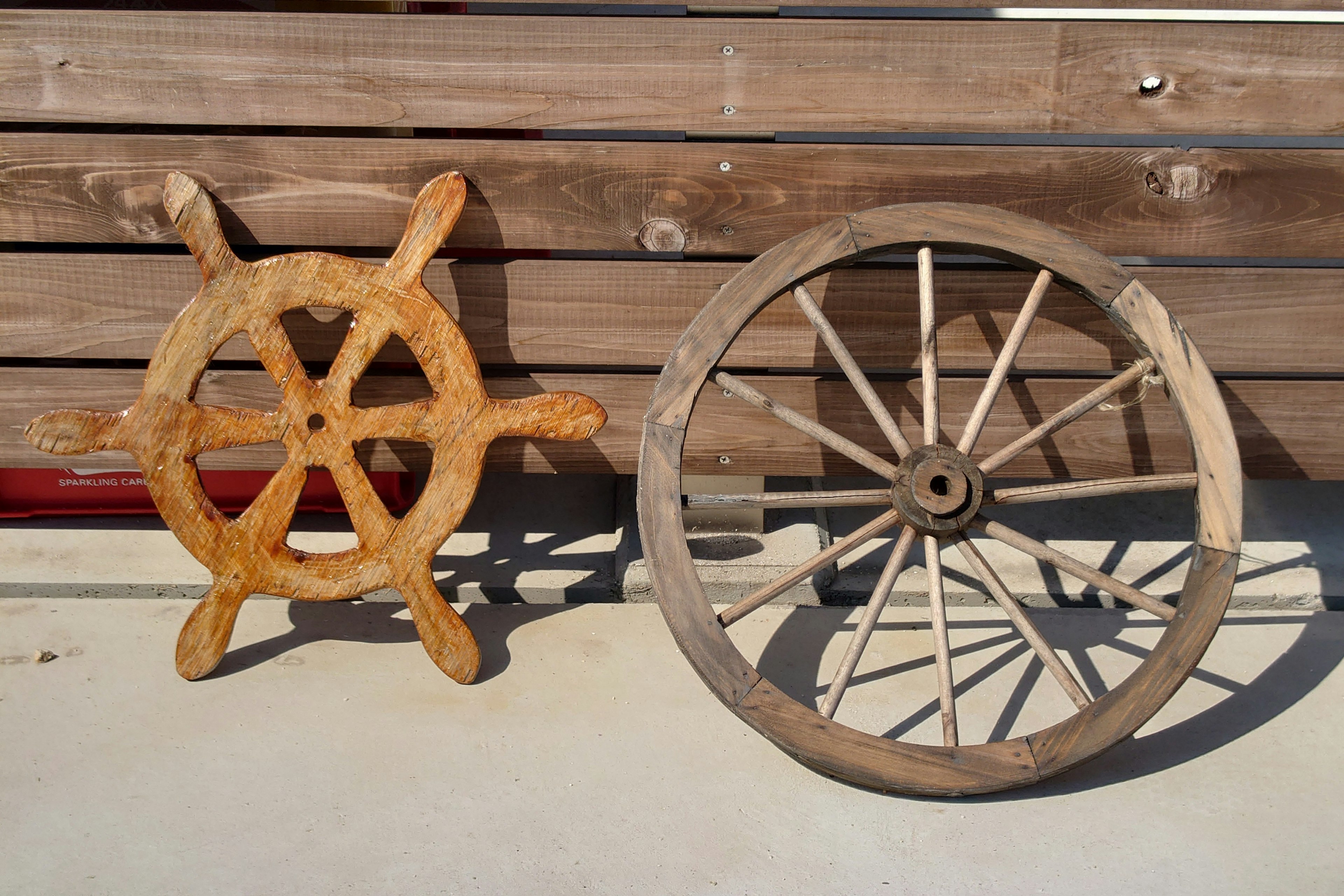 Image of a wooden ship's wheel and a wagon wheel side by side