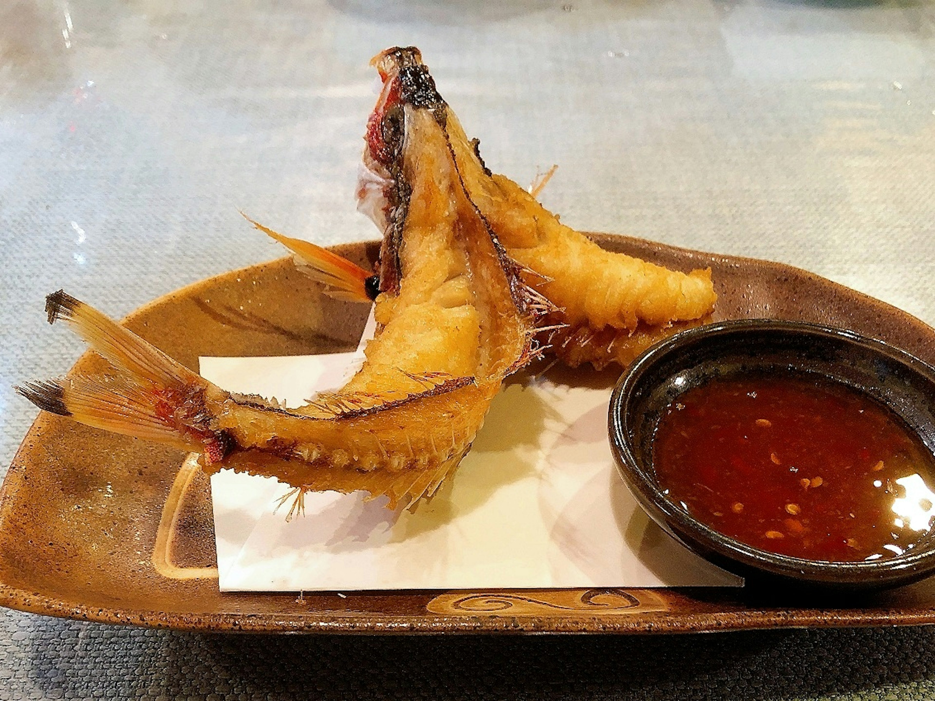 Cabeza de pescado frito servida en un plato con salsa para mojar