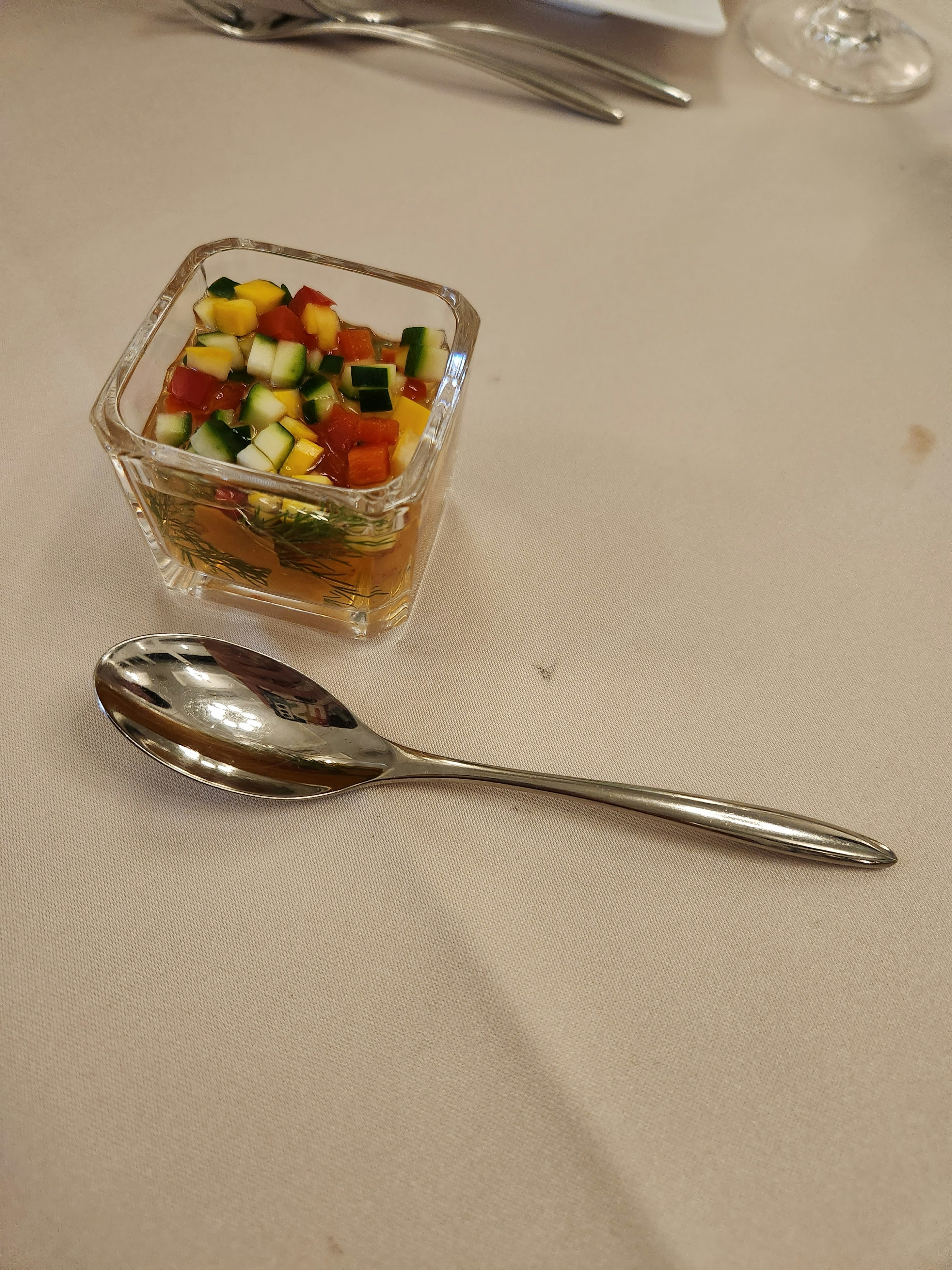 Colorful salad in a clear container with a silver spoon beside it