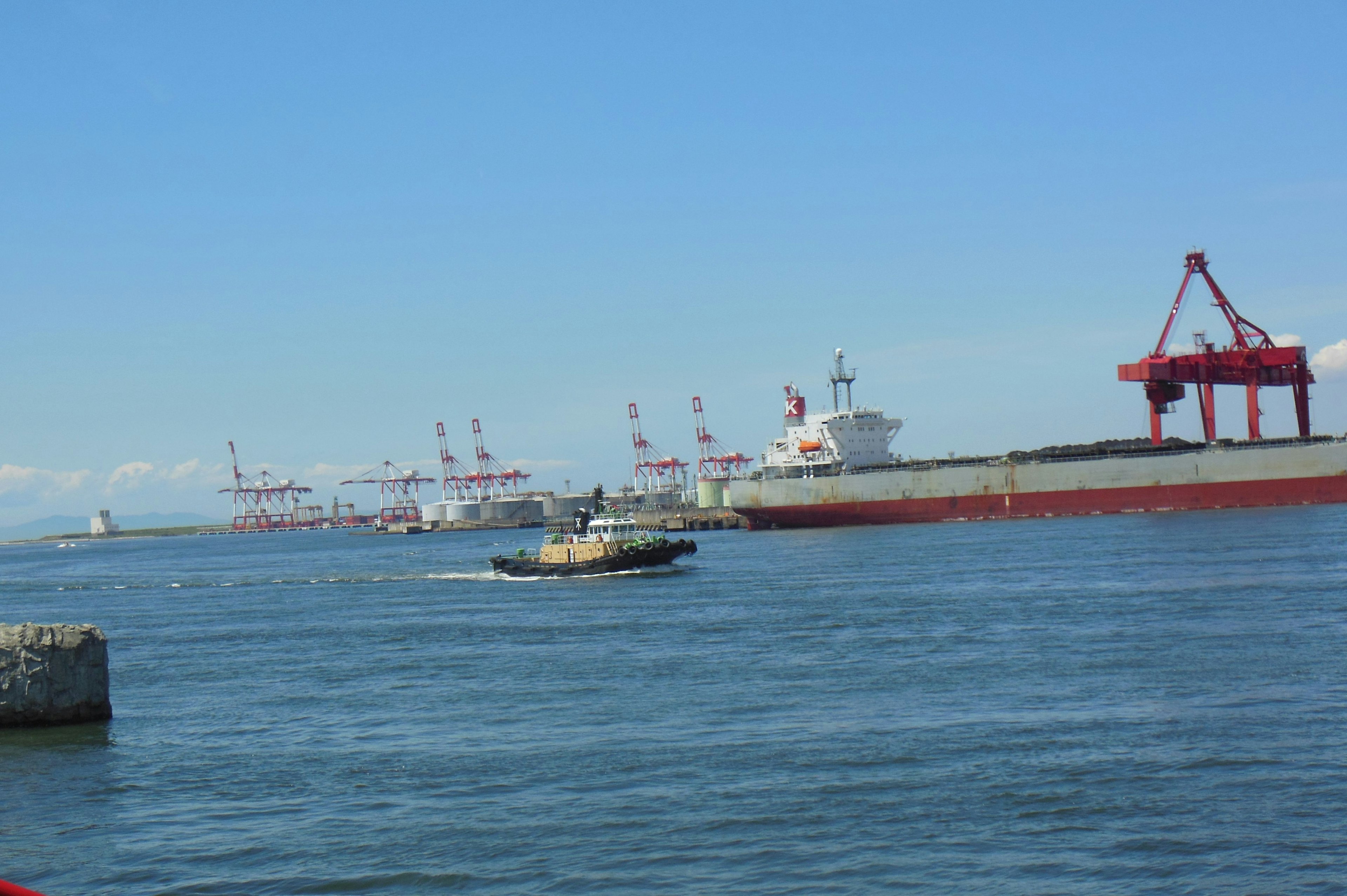 Scene of large cargo ships docked at the port with a small boat navigating the water