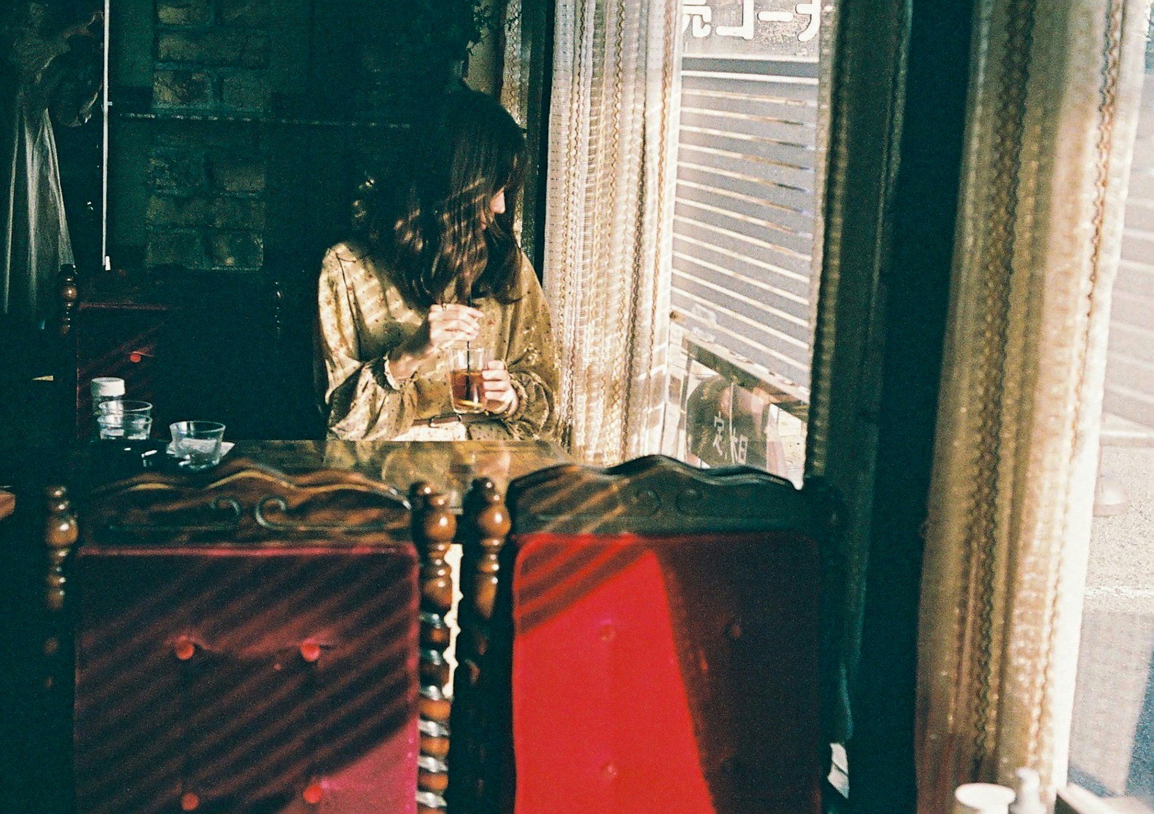 Woman holding a drink by the window with red chairs in a cozy room