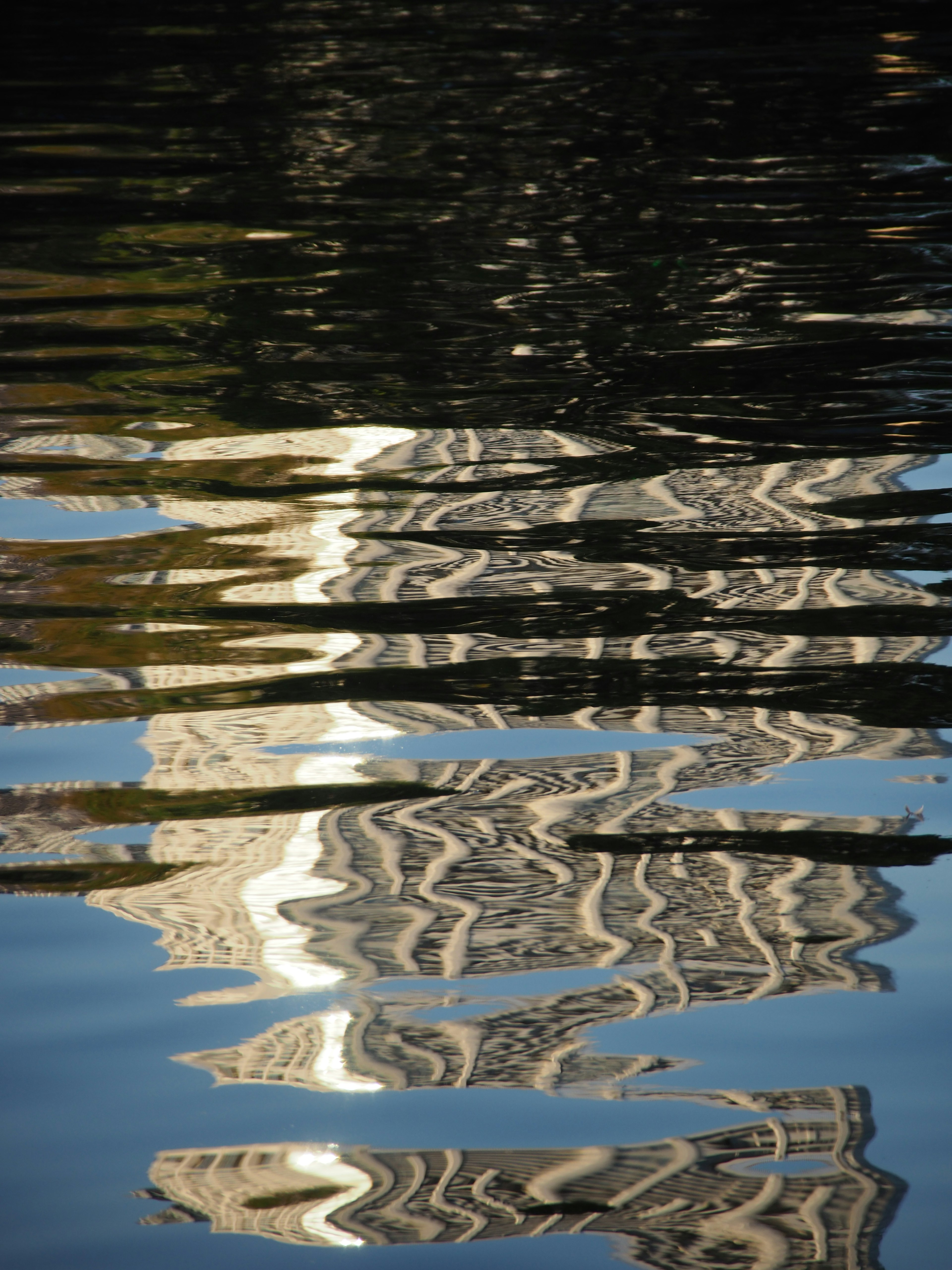 Reflexion eines Gebäudes auf dem Wasser mit Wellen, die ein gewelltes Muster erzeugen