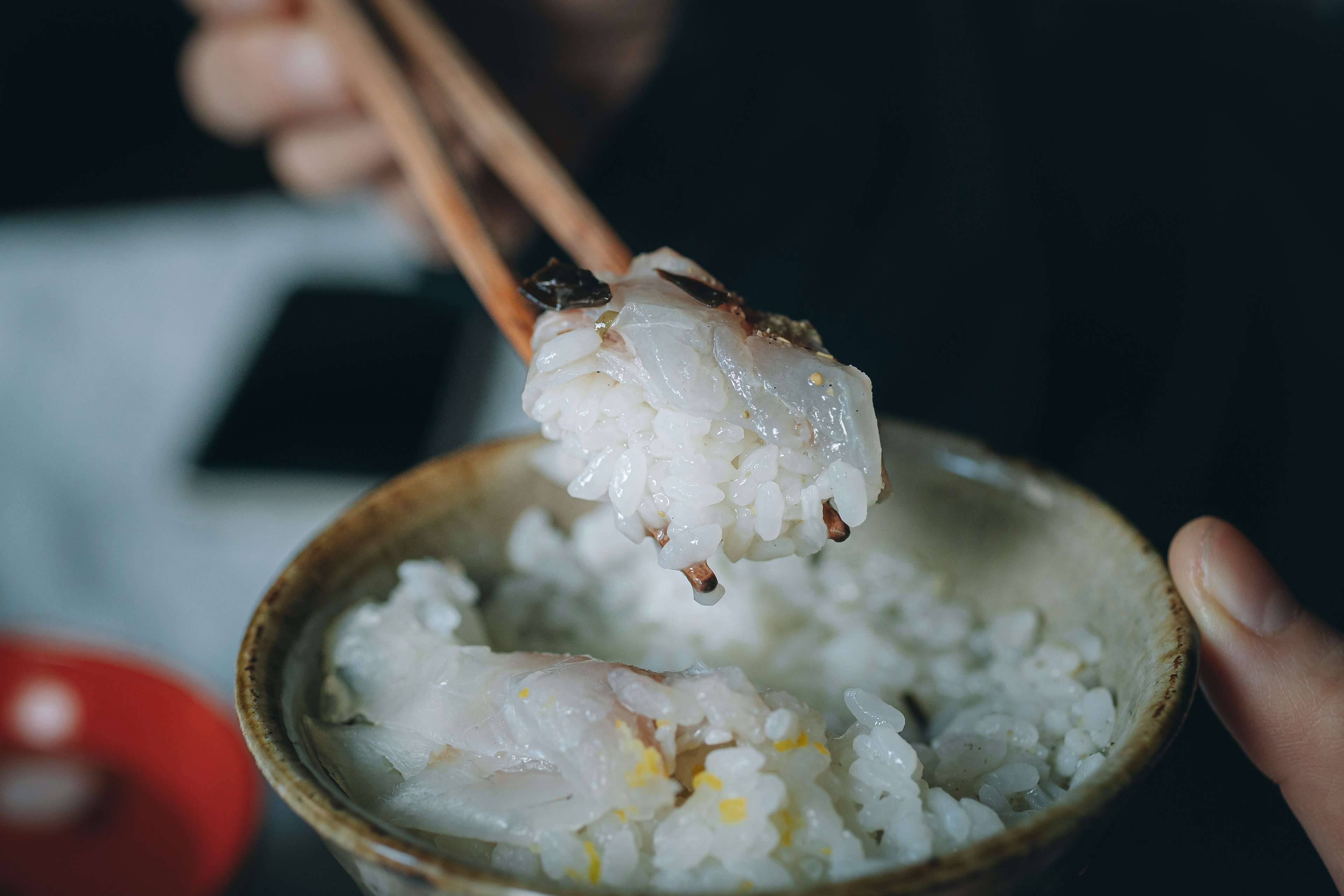 Mano sosteniendo palillos con un tazón de arroz y pescado