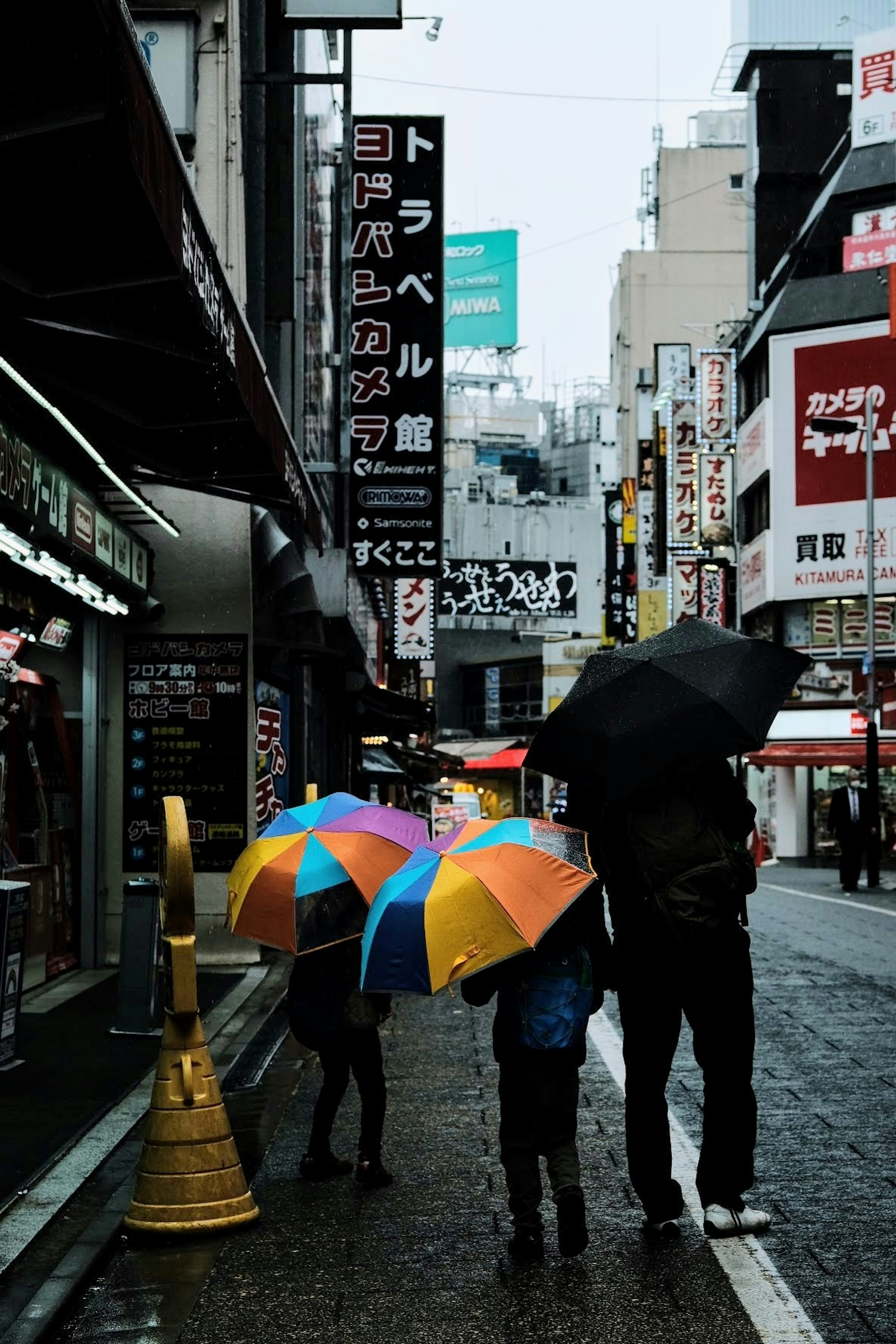 雨の中でカラフルな傘を持つ親子が歩いている街の風景