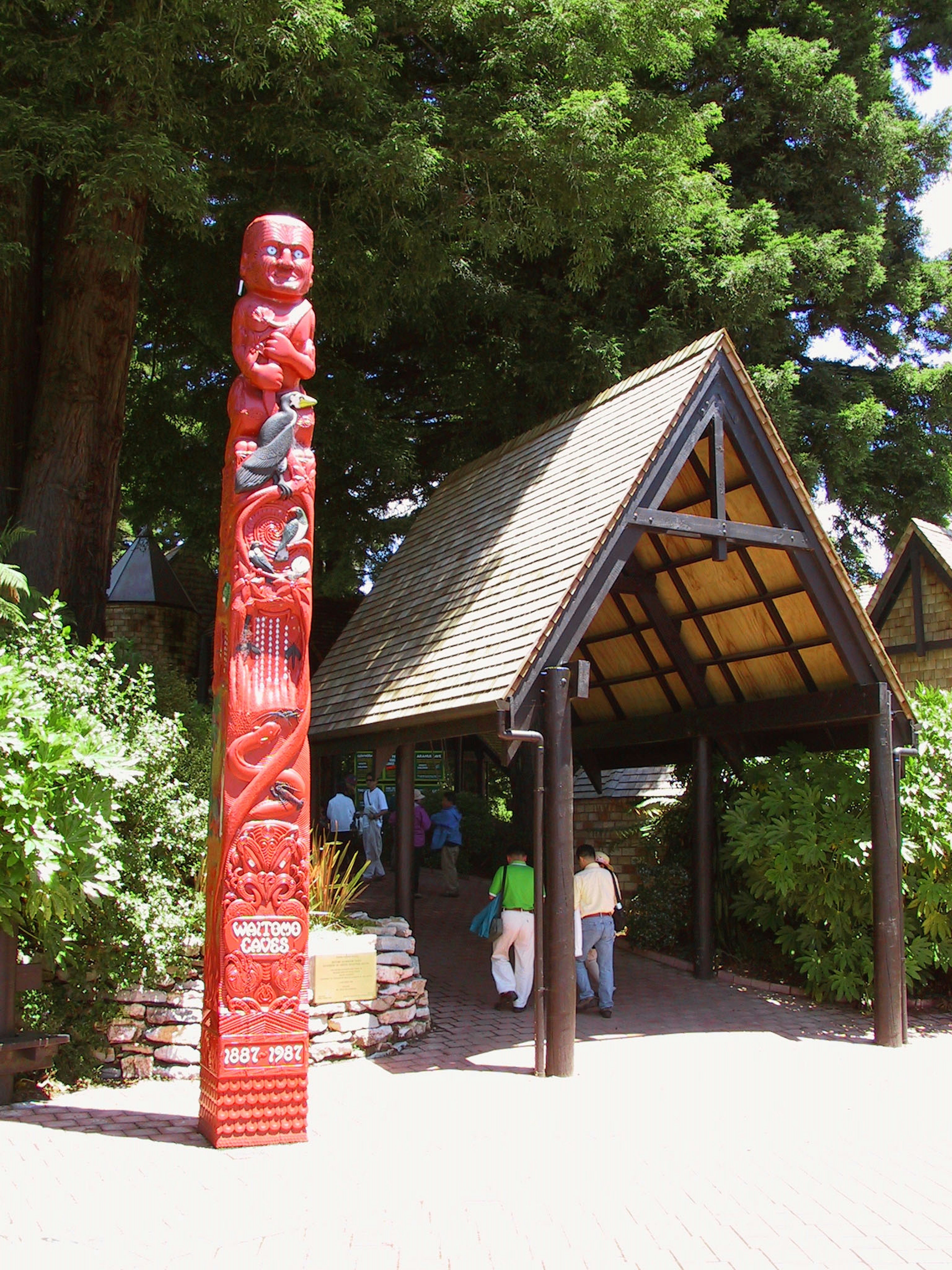 Pohon totem merah di samping bangunan atap jerami yang dikelilingi pepohonan