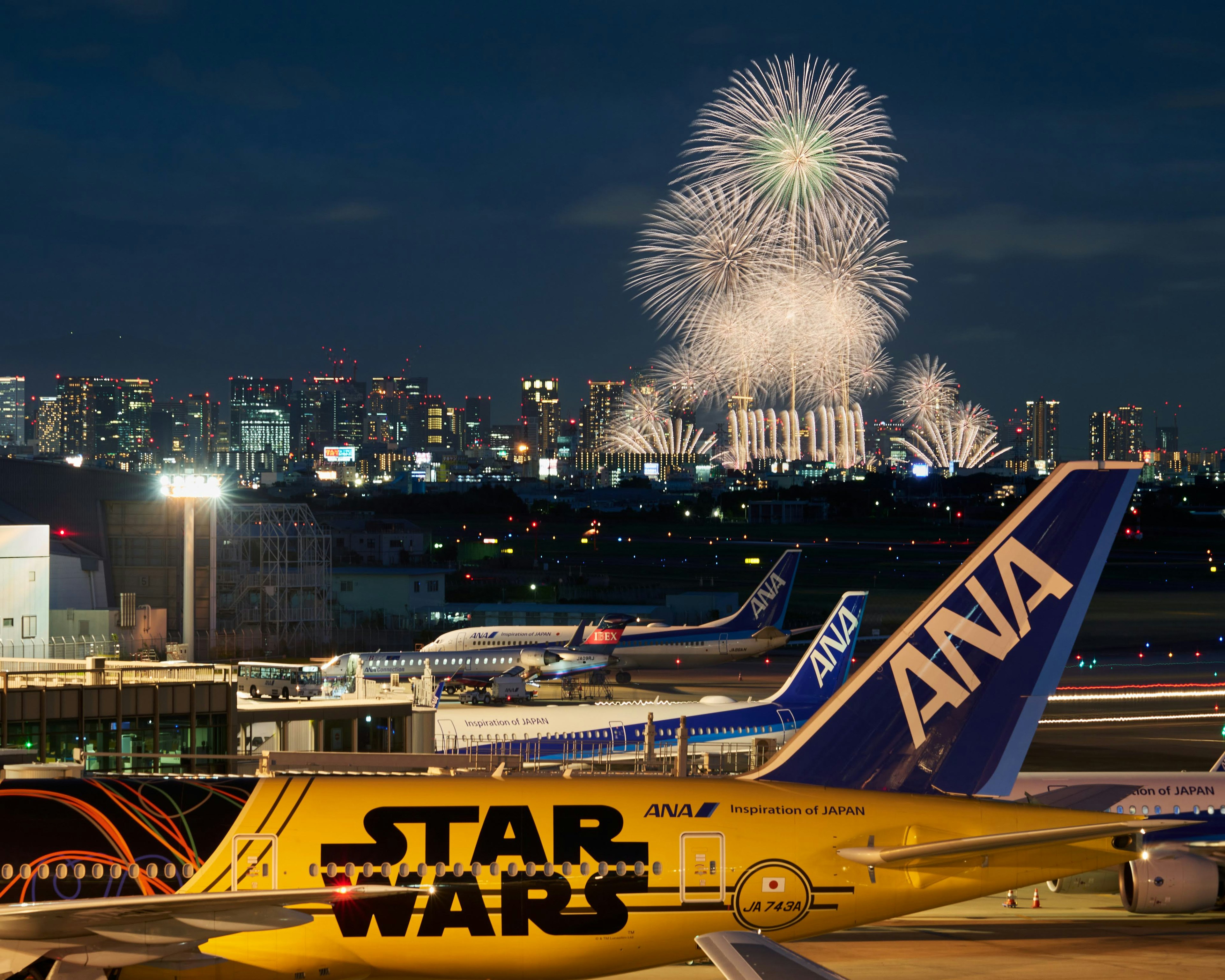 Pesawat dengan logo Star Wars dan livery ANA di bandara Tokyo dengan kembang api di langit malam