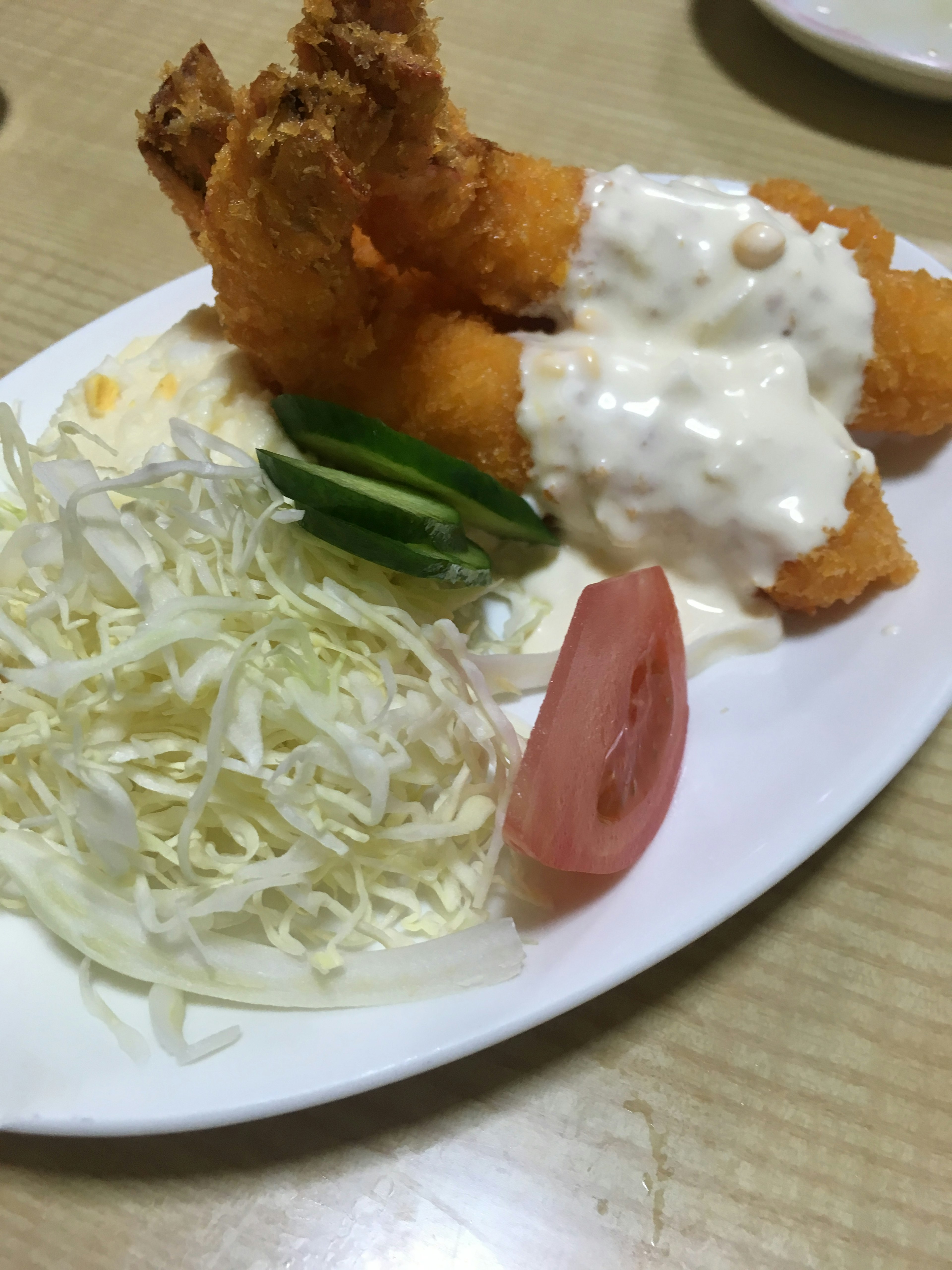 Fried shrimp with creamy sauce served on a white plate accompanied by cabbage and tomato