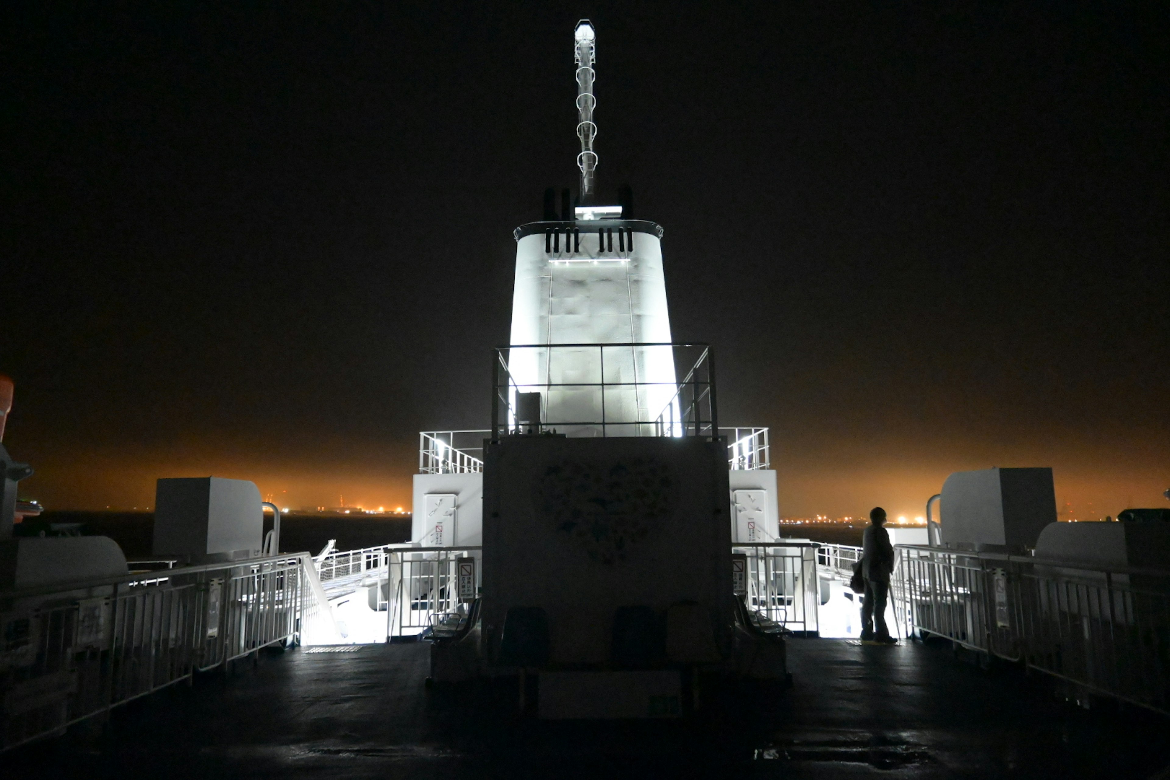 Faro bianco illuminato di notte con una figura in silhouette