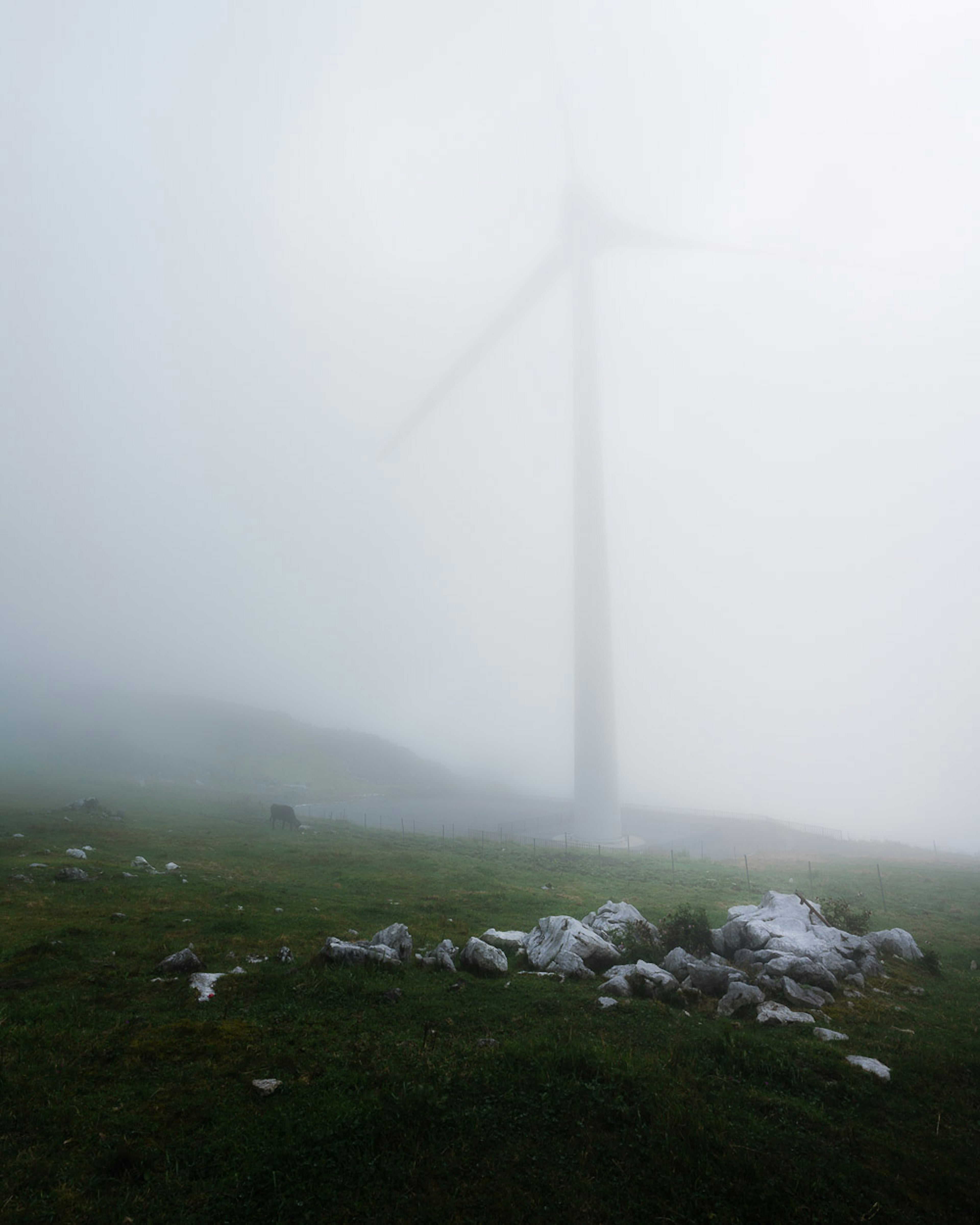 Wind turbine shrouded in fog with rocky terrain