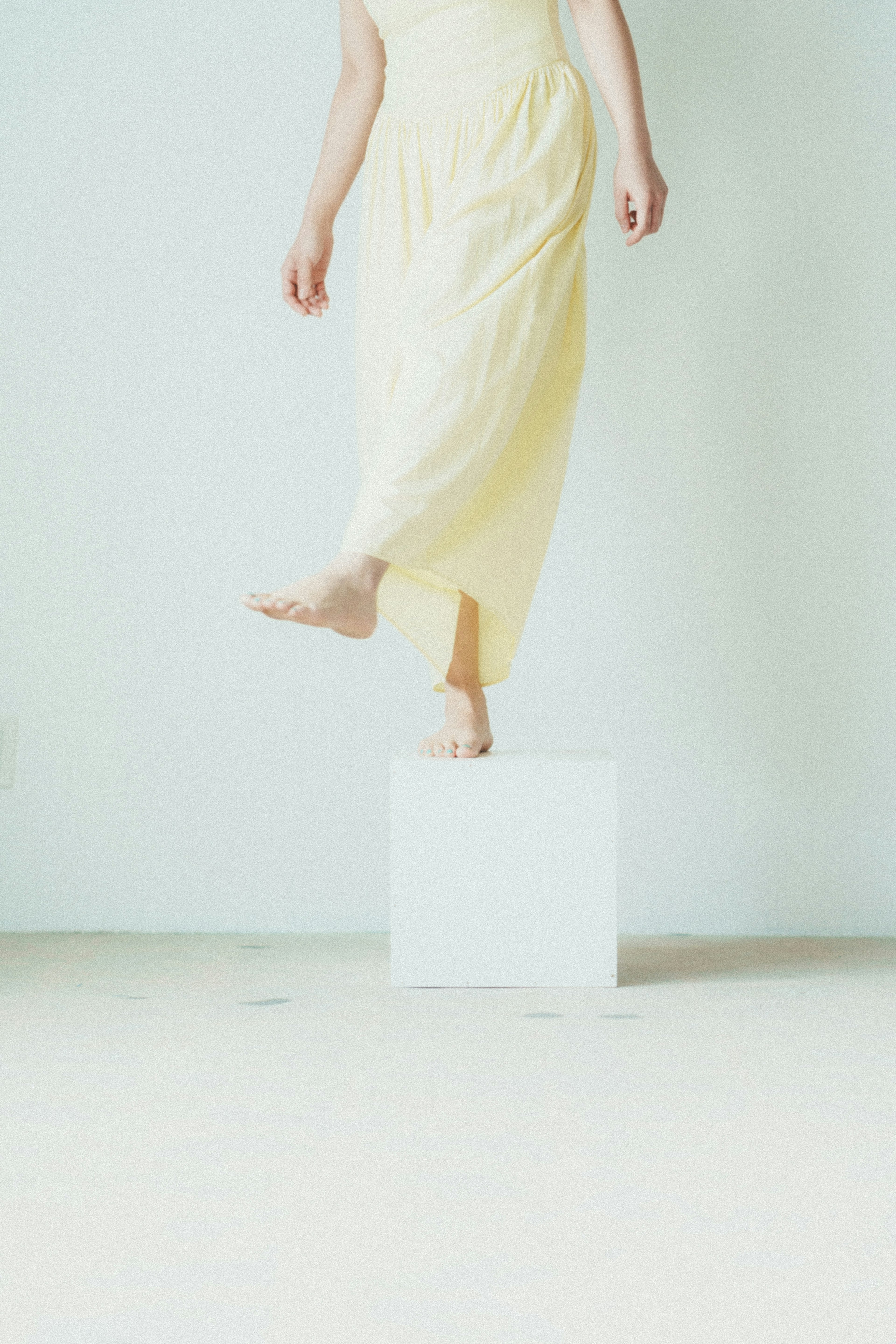 Foto centrada en el pie de una mujer pisando un pedestal blanco con un vestido amarillo suave