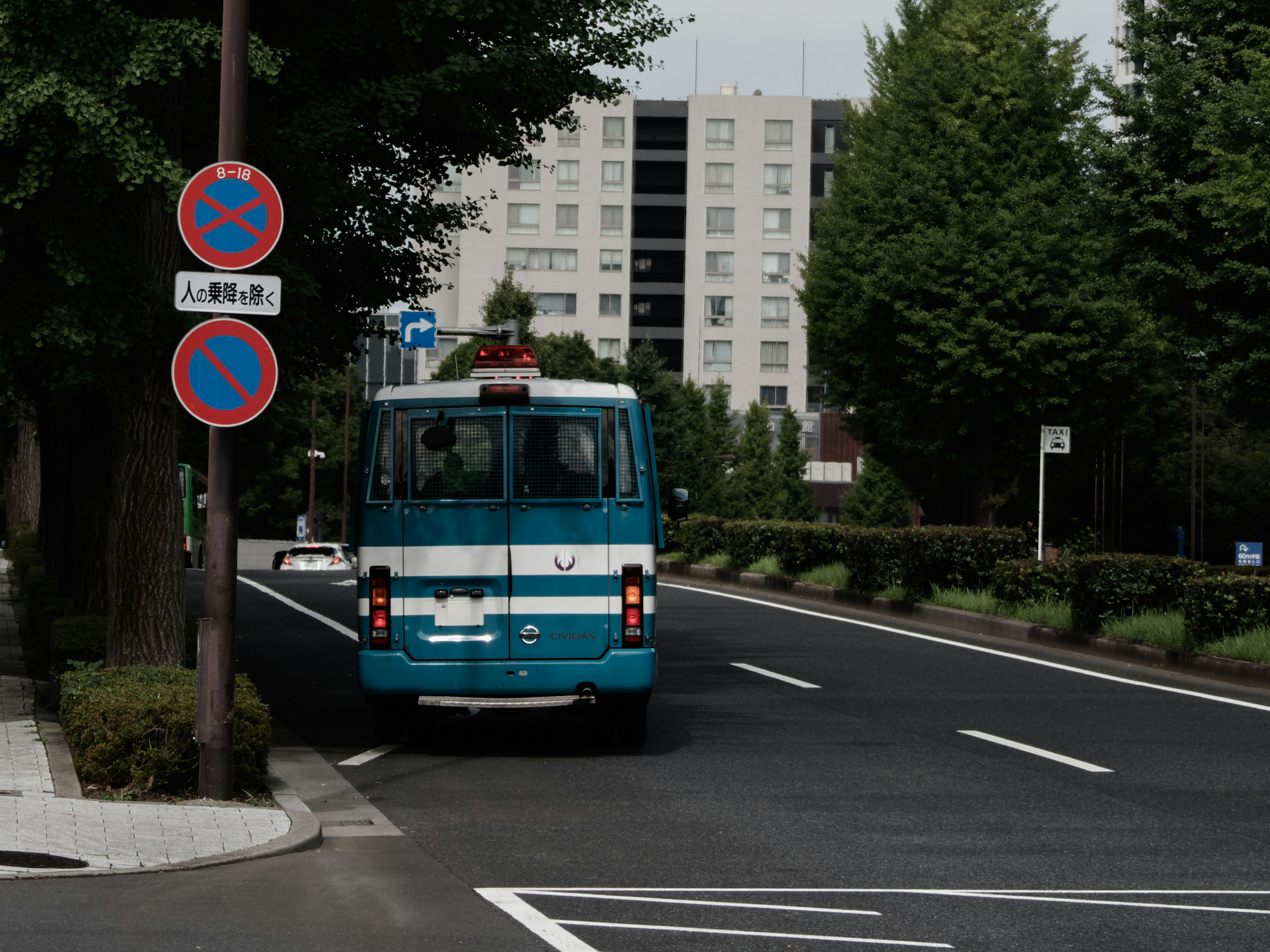 青いバスが街路を走る様子が見える周囲に緑の木々が並ぶ