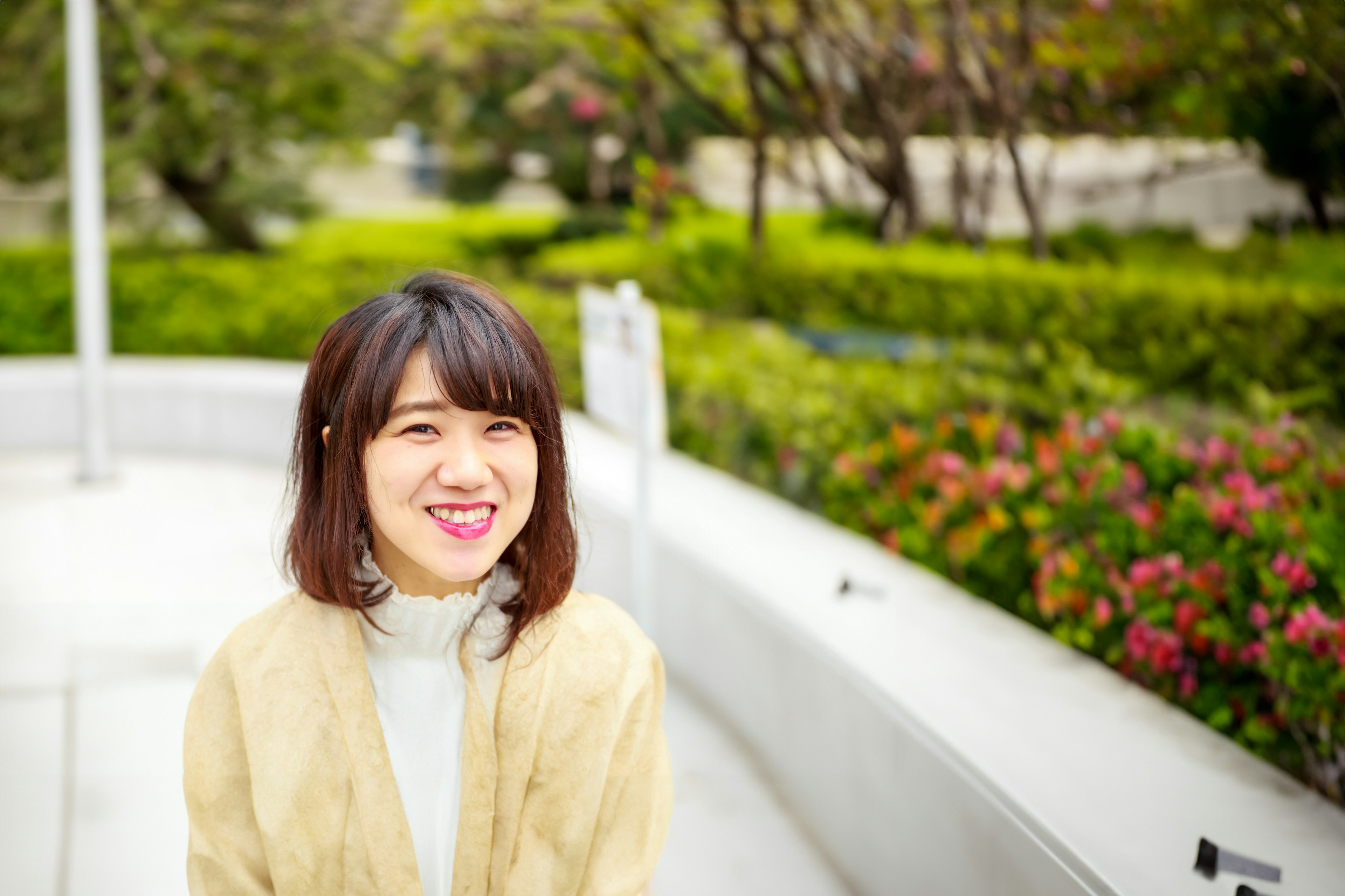 Portrait of a smiling woman in a park with greenery and flowers in the background