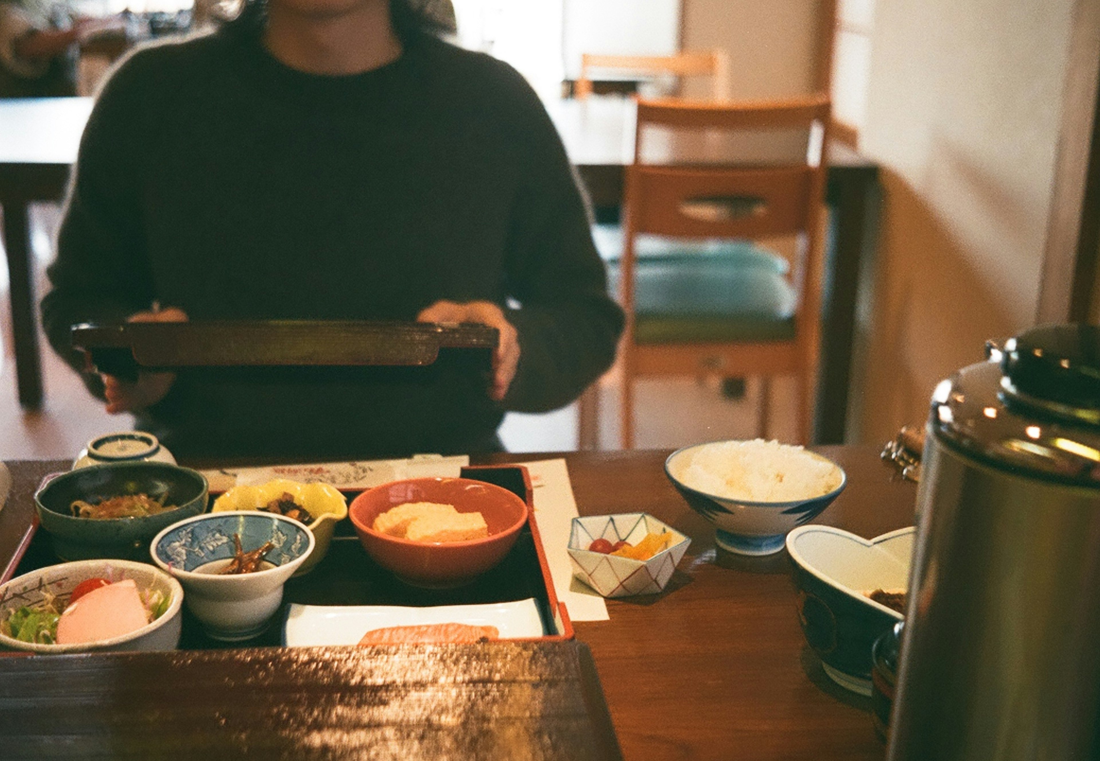 Person hält ein Tablett mit japanischem Essen auf einem Holztisch