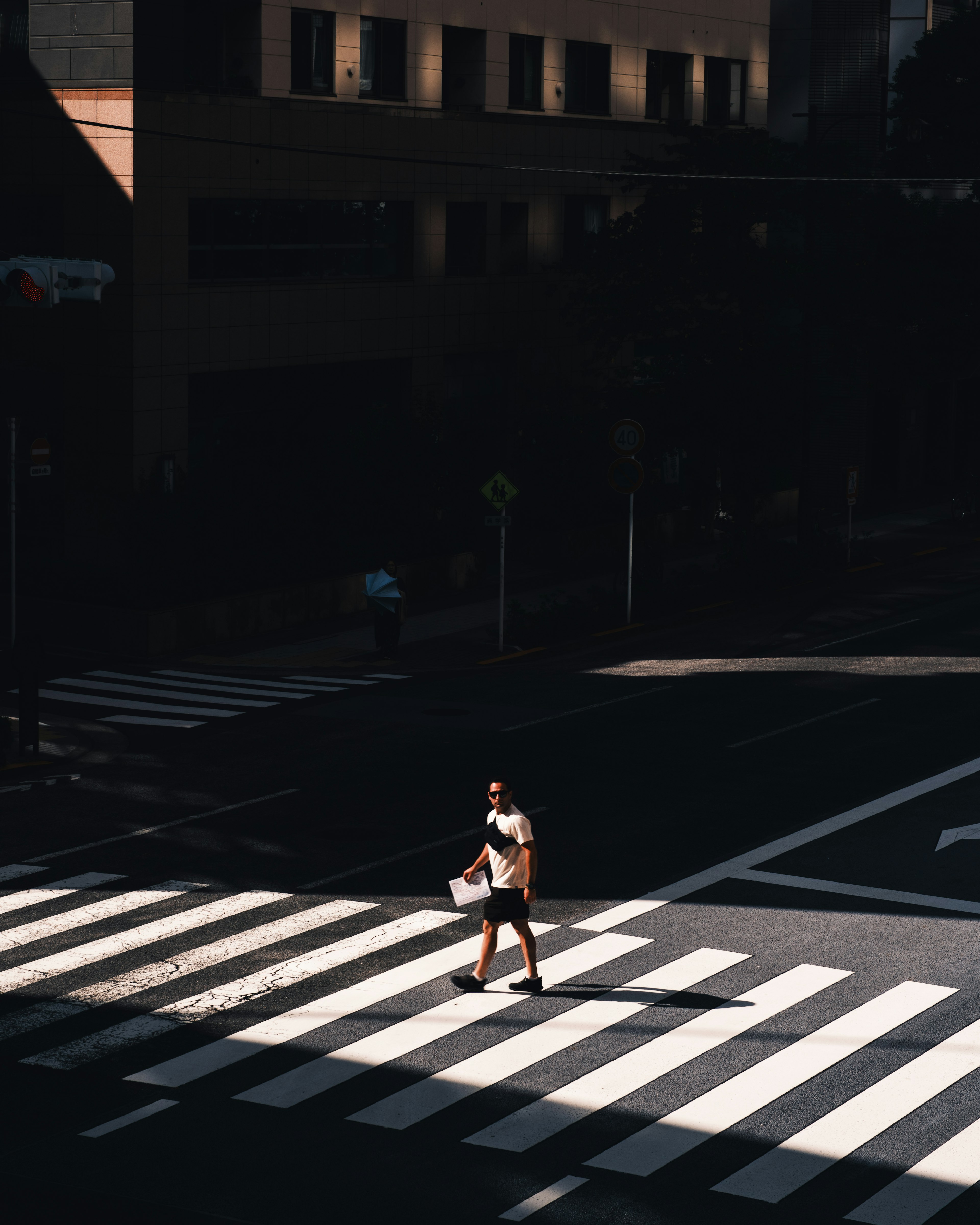 A figure crossing a pedestrian crosswalk with strong light and shadow contrasts