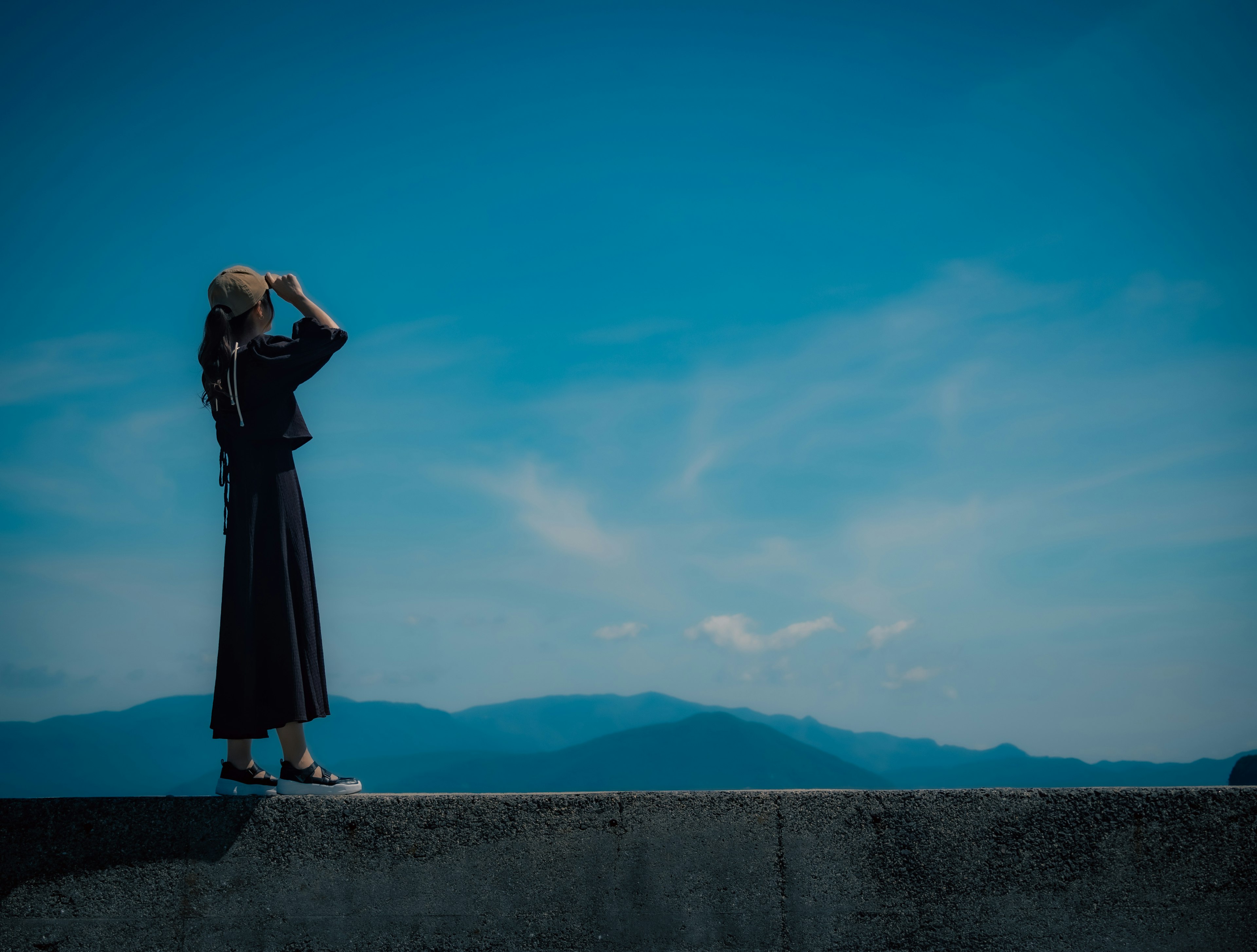 青空の下で遠くを見つめる女性のシルエット