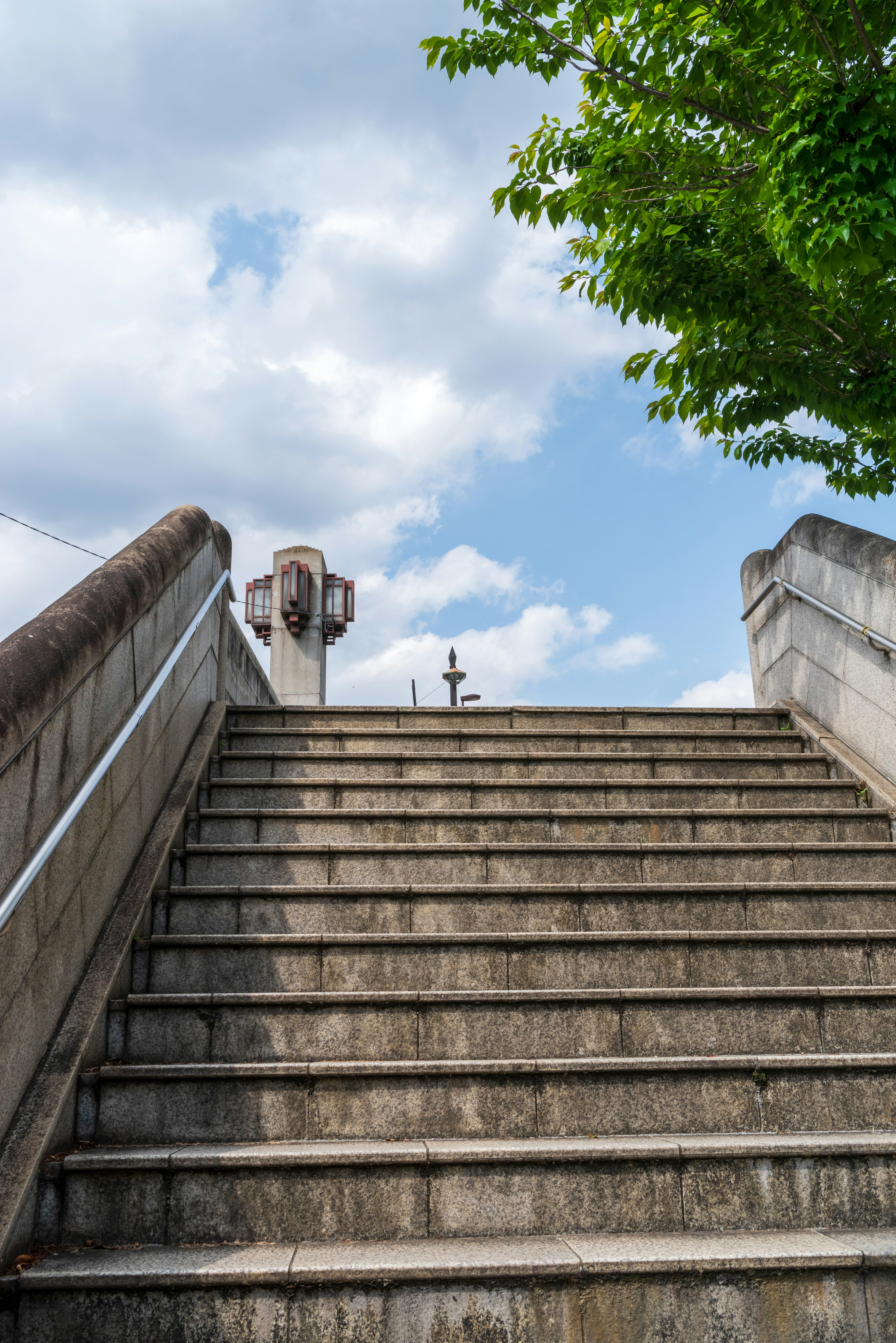 Staircase leading up to a blue sky with clouds and greenery