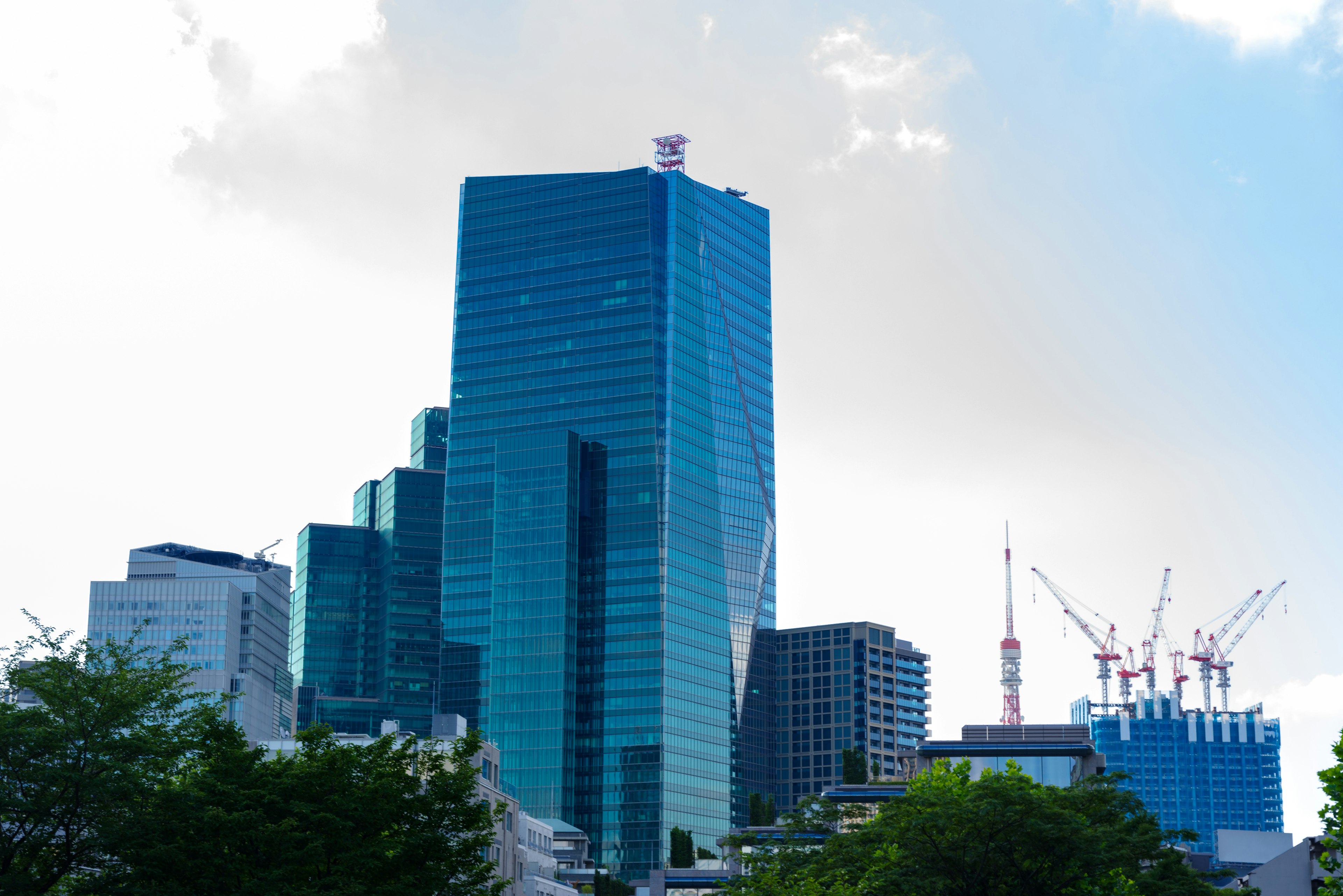 Urban skyline featuring a tall glass building and construction cranes