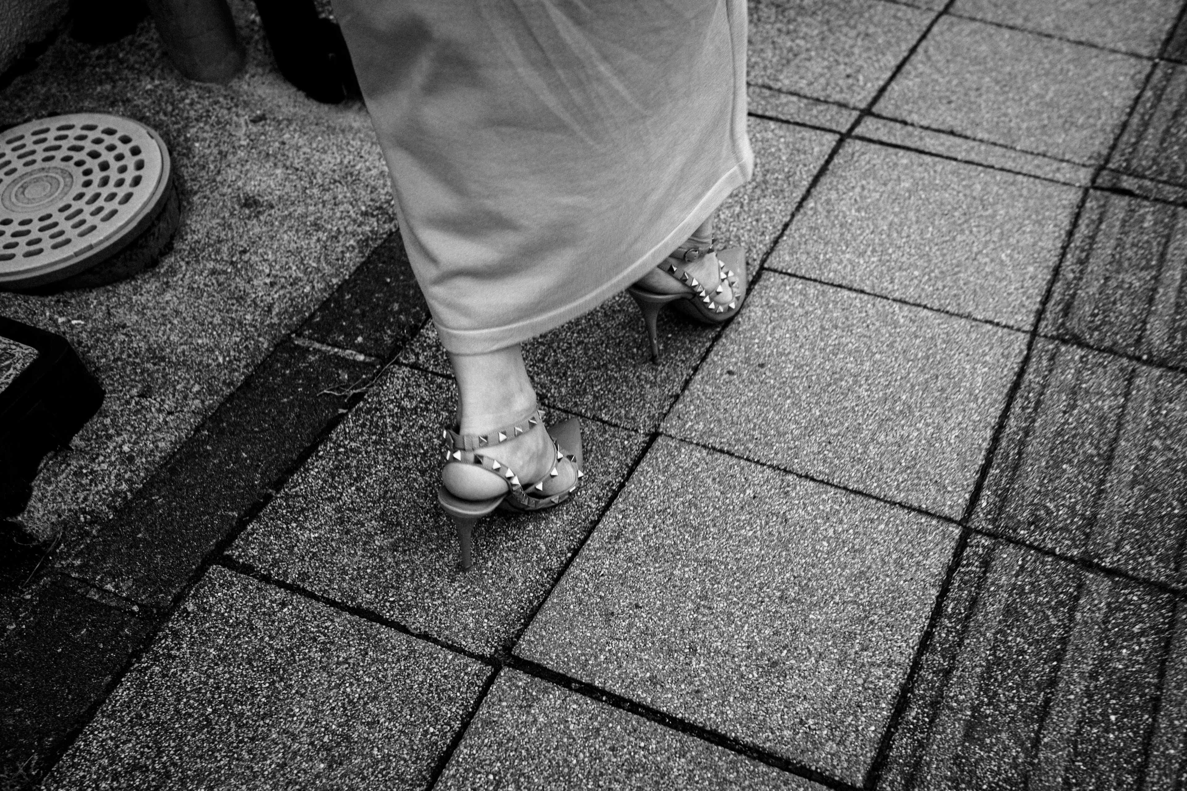 A person walking in high heels on a pavement in black and white