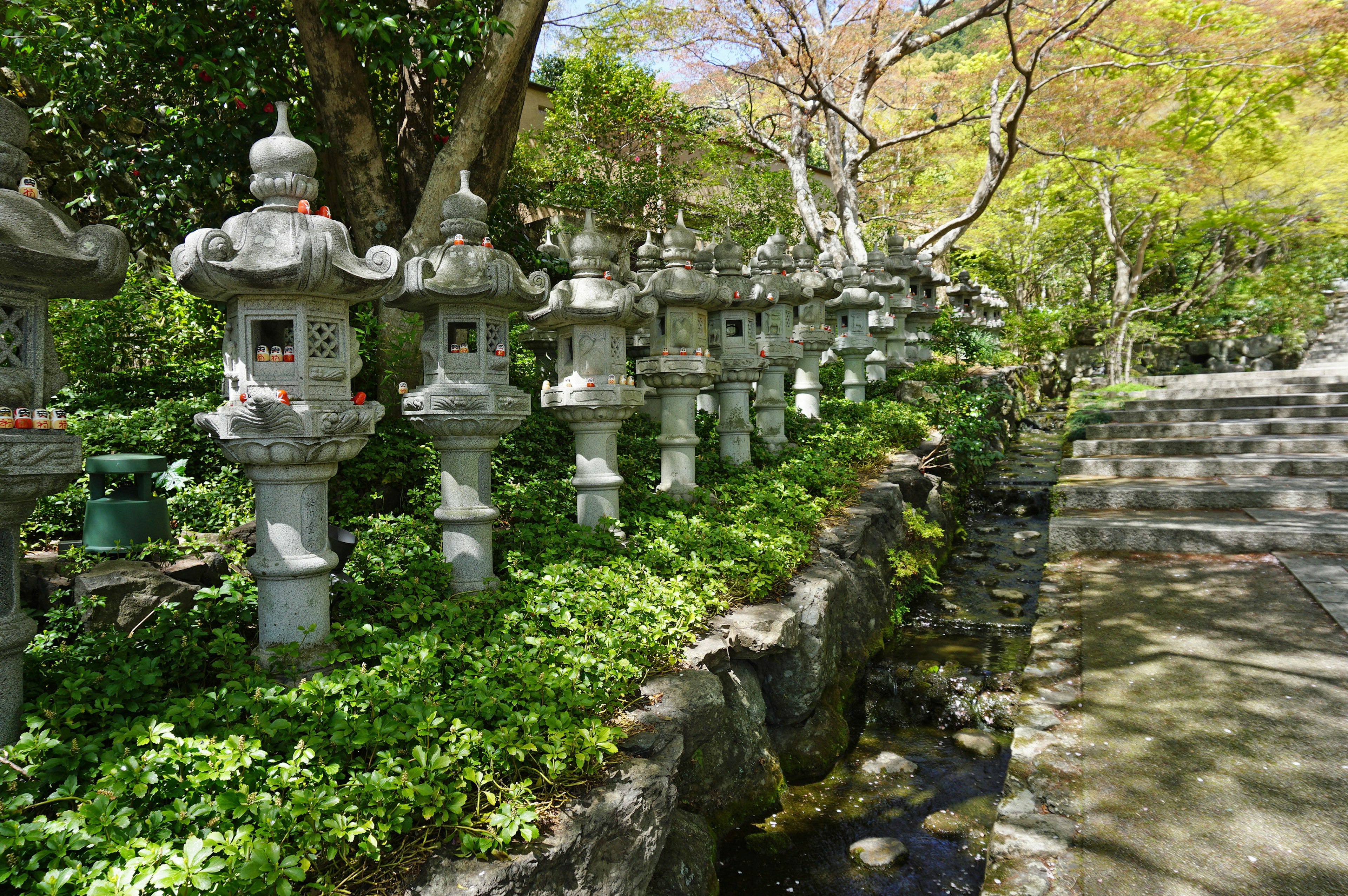 石燈籠排成一排，旁邊是郁郁蔥蔥的花園和流動的小溪