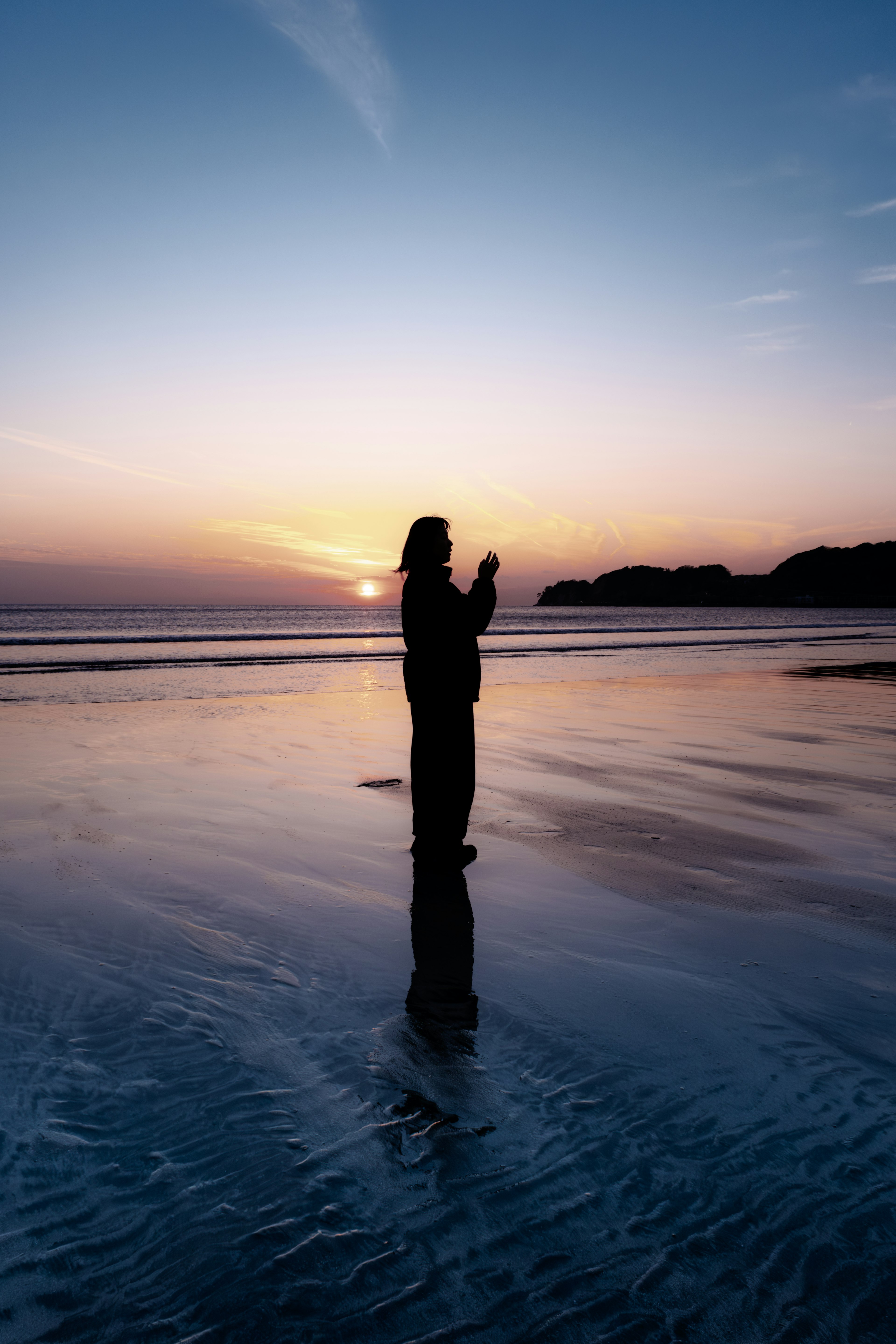 Silhouette d'une personne se tenant au bord de la plage au coucher du soleil