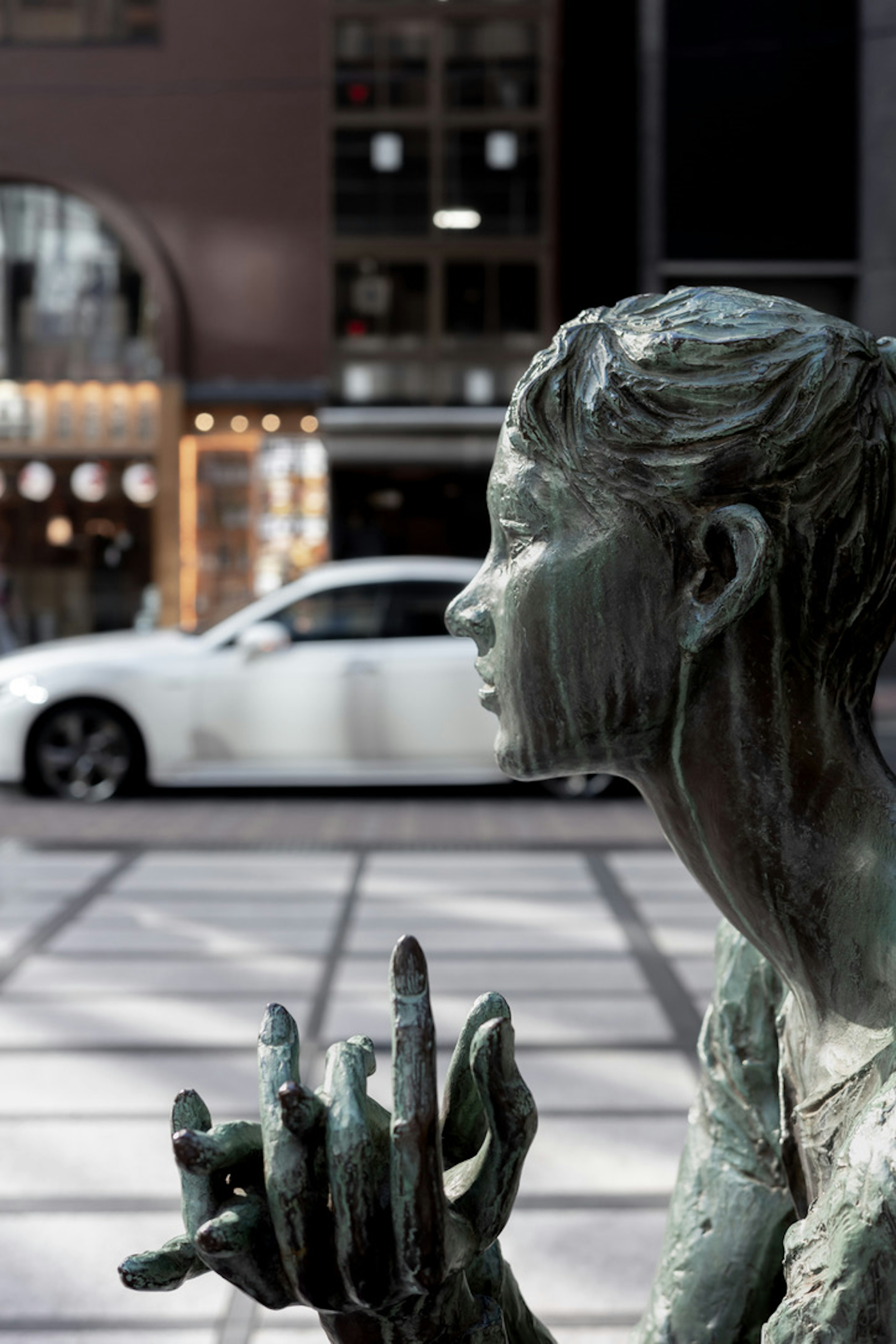 Bronze female statue with a white car and modern buildings in the background