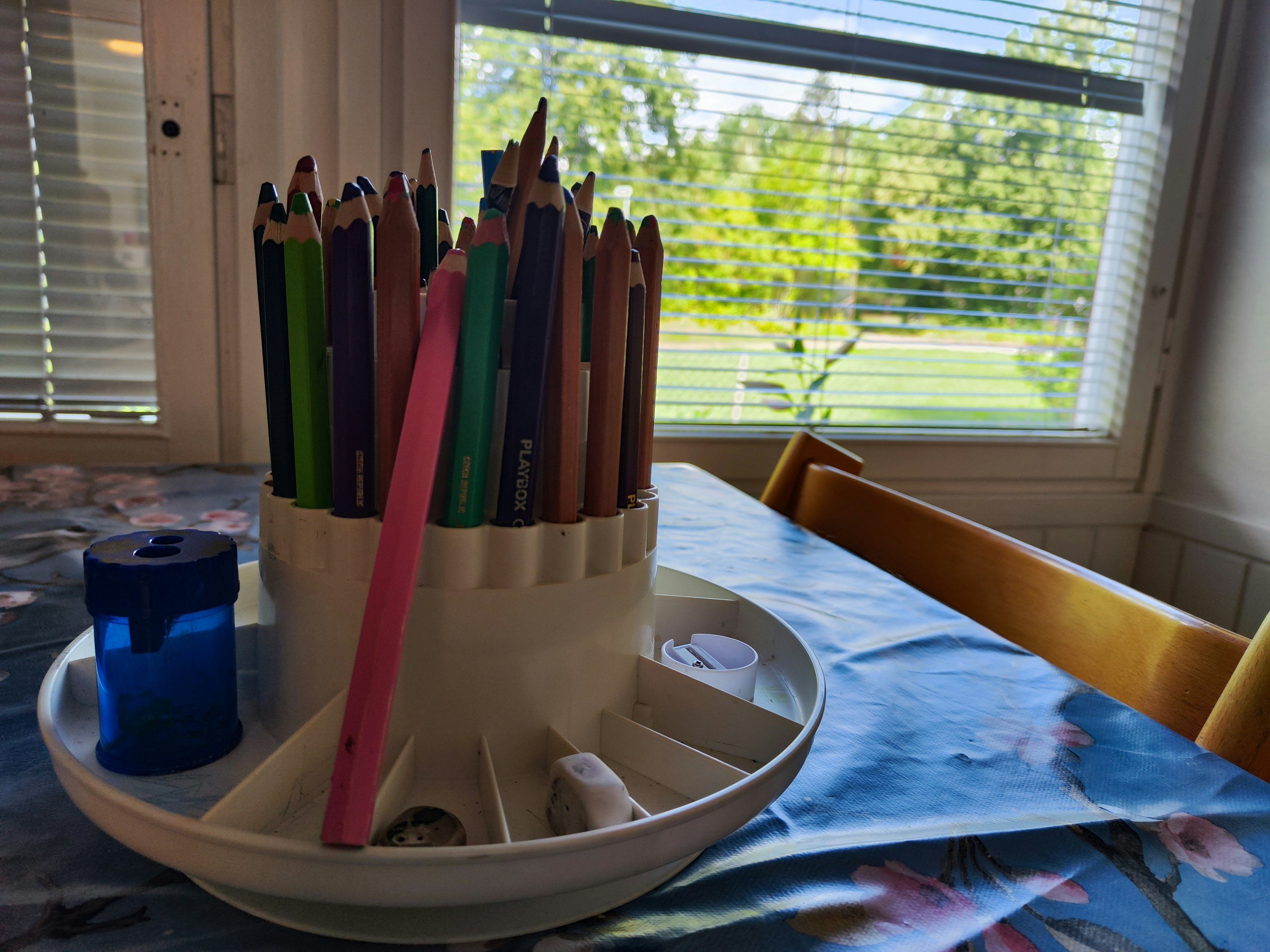 Colorful colored pencils in a holder with a blue sharpener on a table