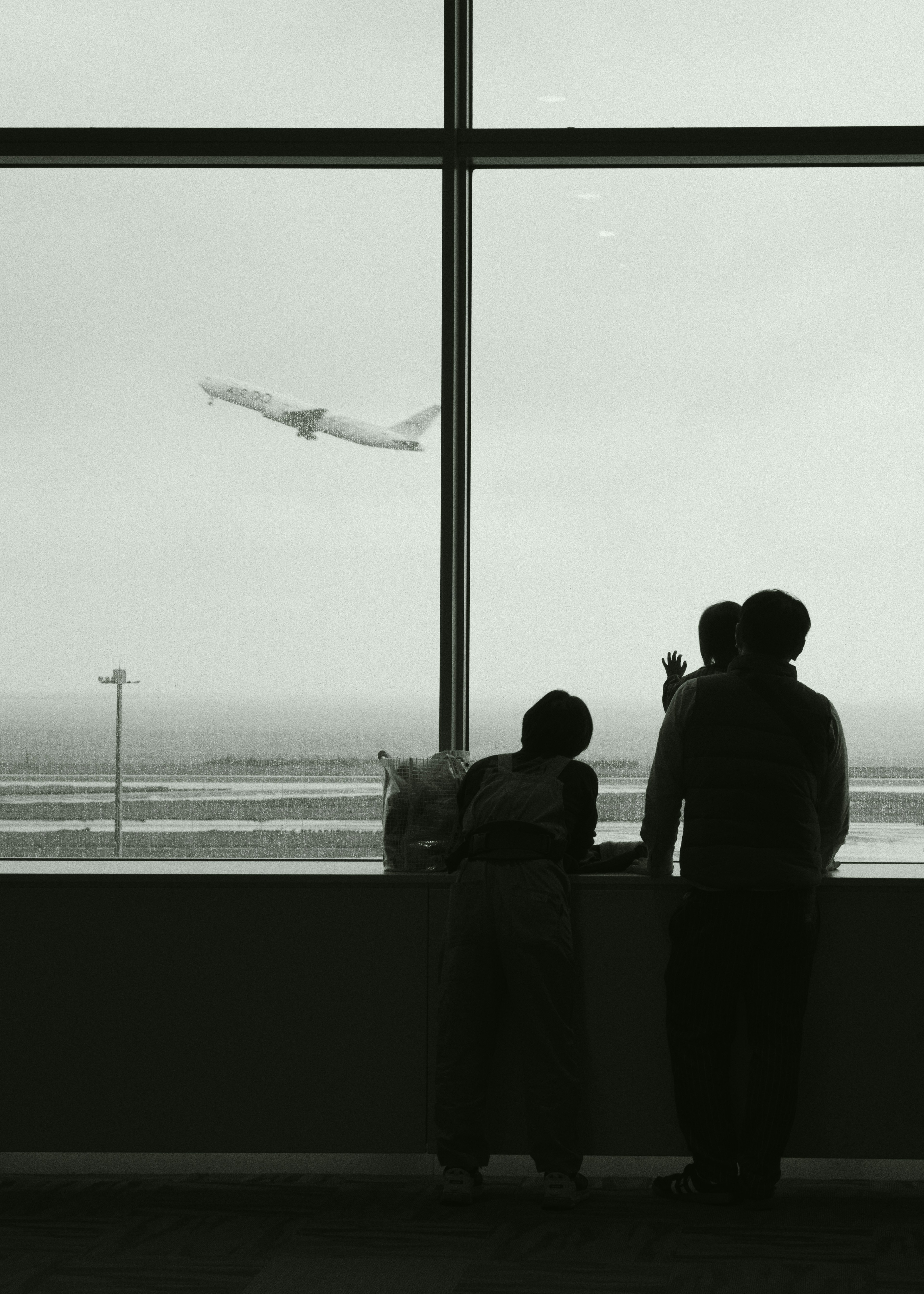 Due persone in piedi accanto a una finestra dell'aeroporto che guardano un aereo decollare