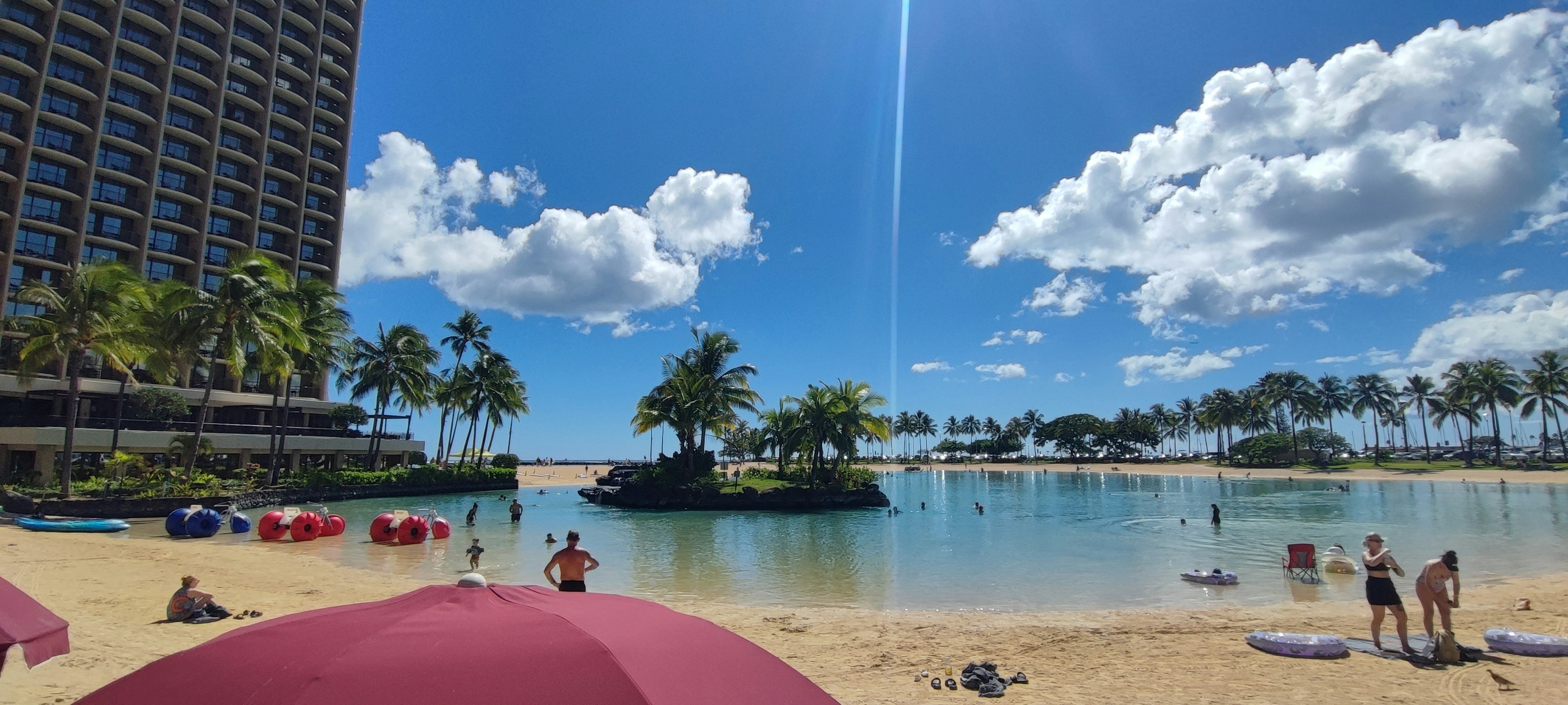 Vista della spiaggia con cielo blu nuvole bianche palme e ombrelloni rossi