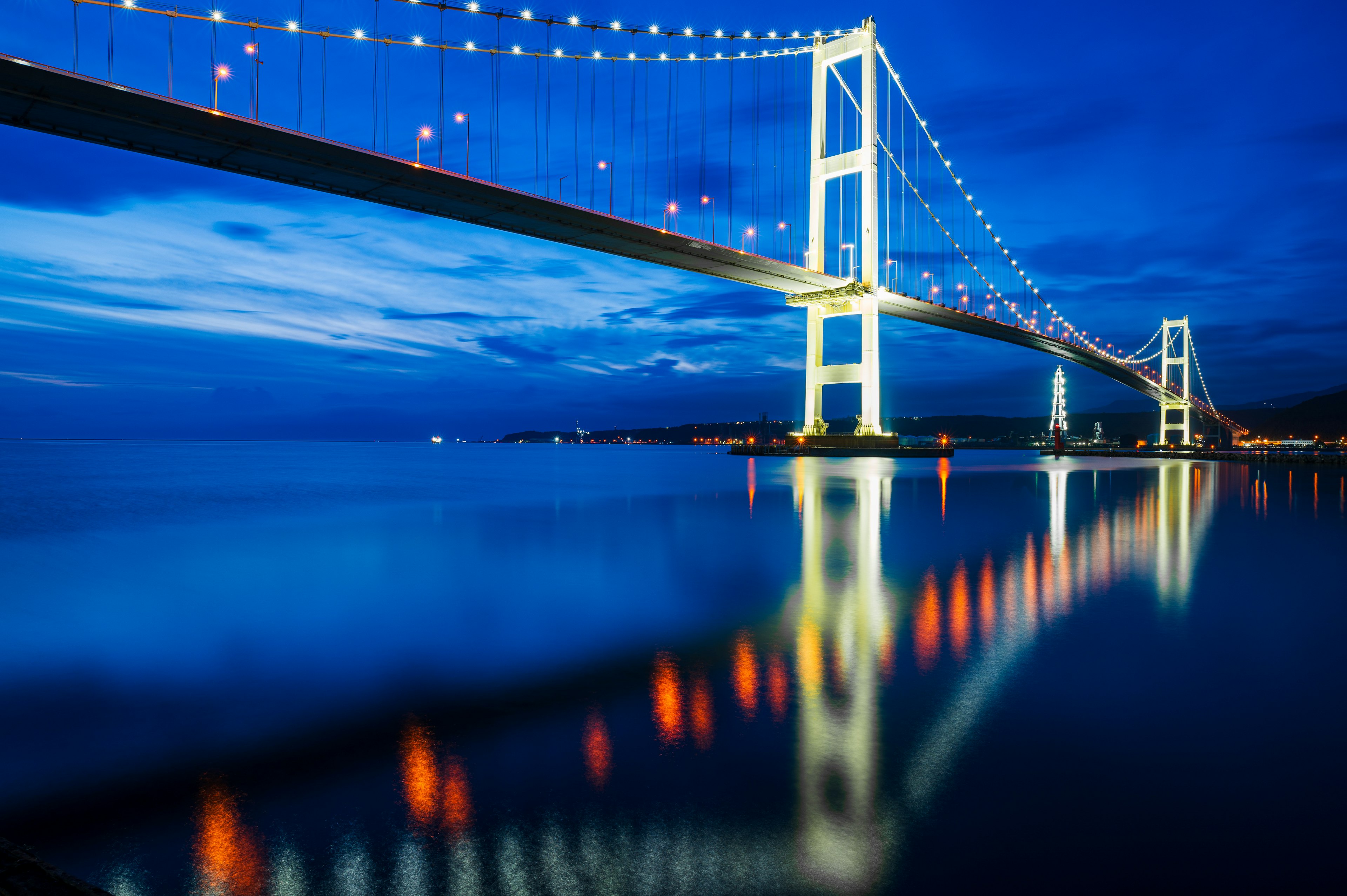 Vue magnifique d'un pont illuminé sous un ciel nocturne bleu avec des reflets sur l'eau