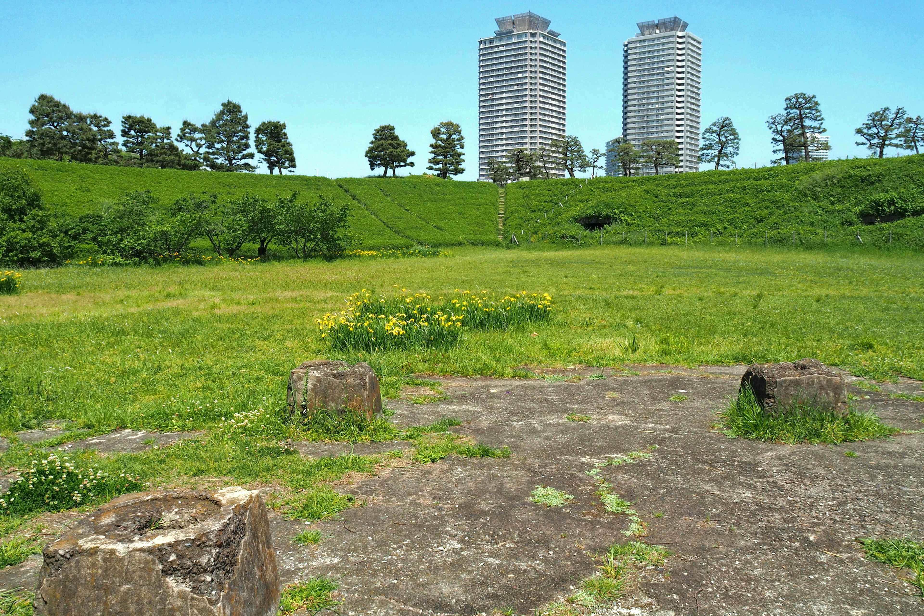 A concrete foundation surrounded by green grass with high-rise buildings in the background