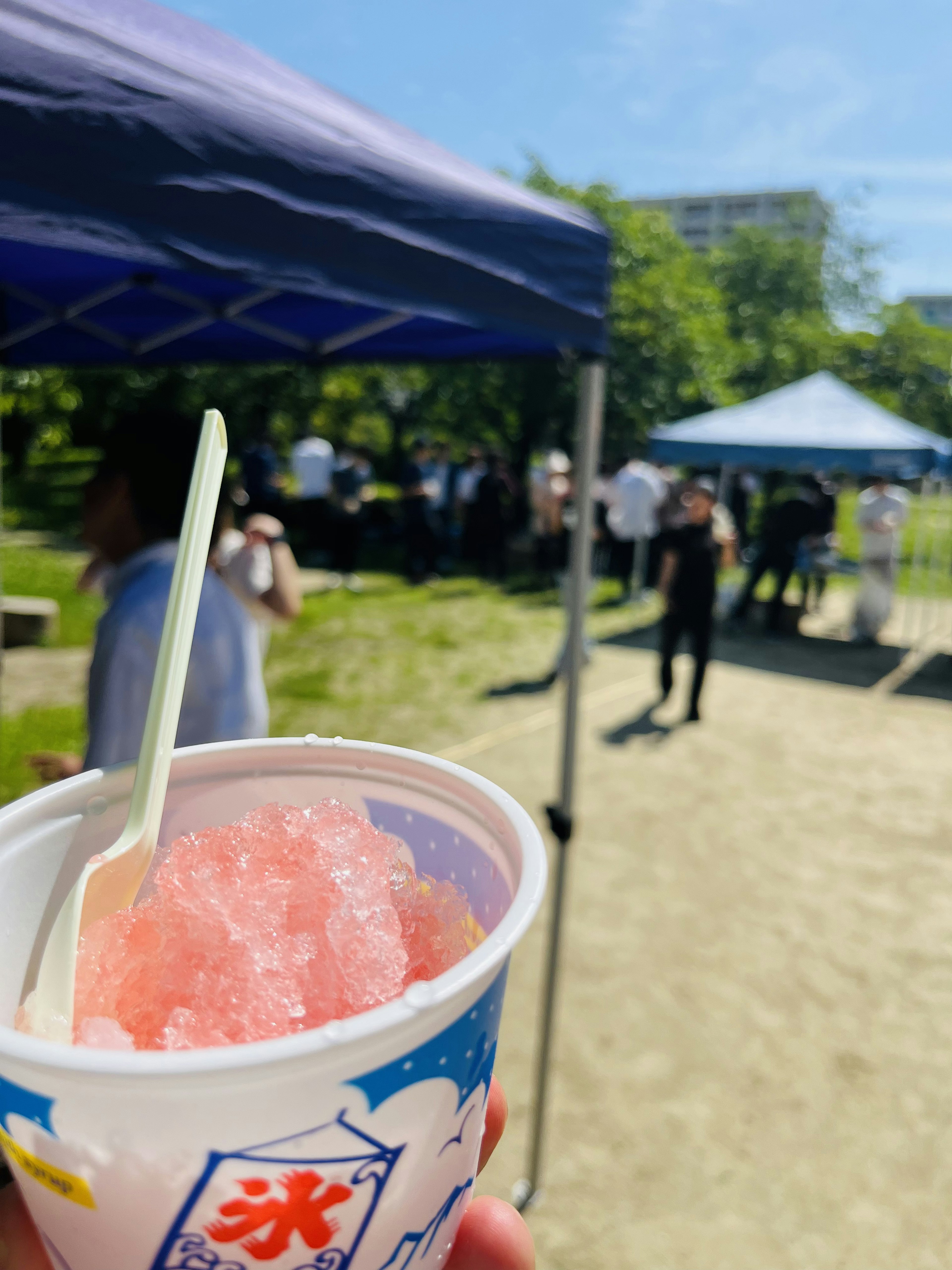 公園でかき氷を持つ手と背景のテント