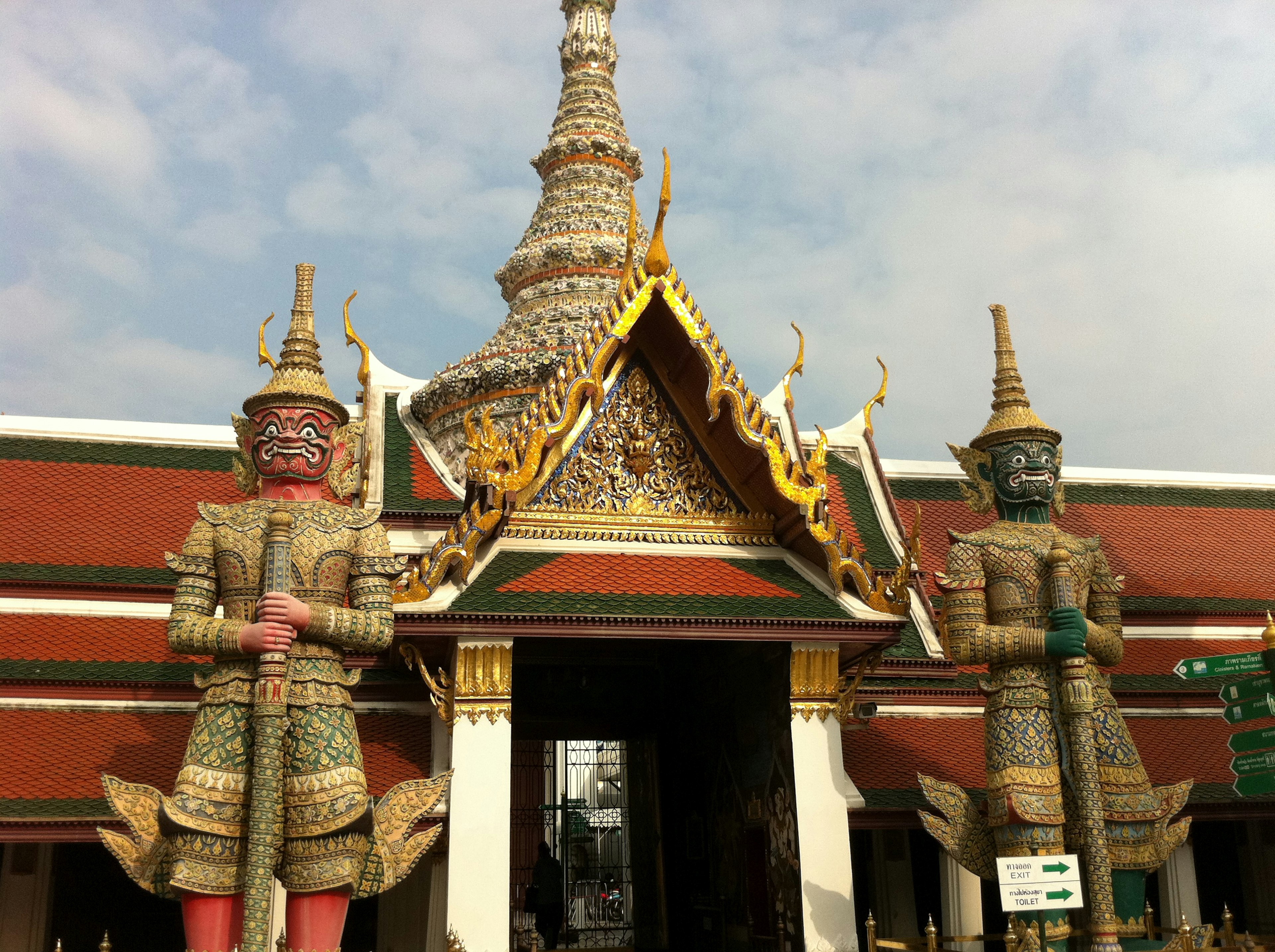 Entrance of a Bangkok temple featuring two giant guardian statues and ornate roof