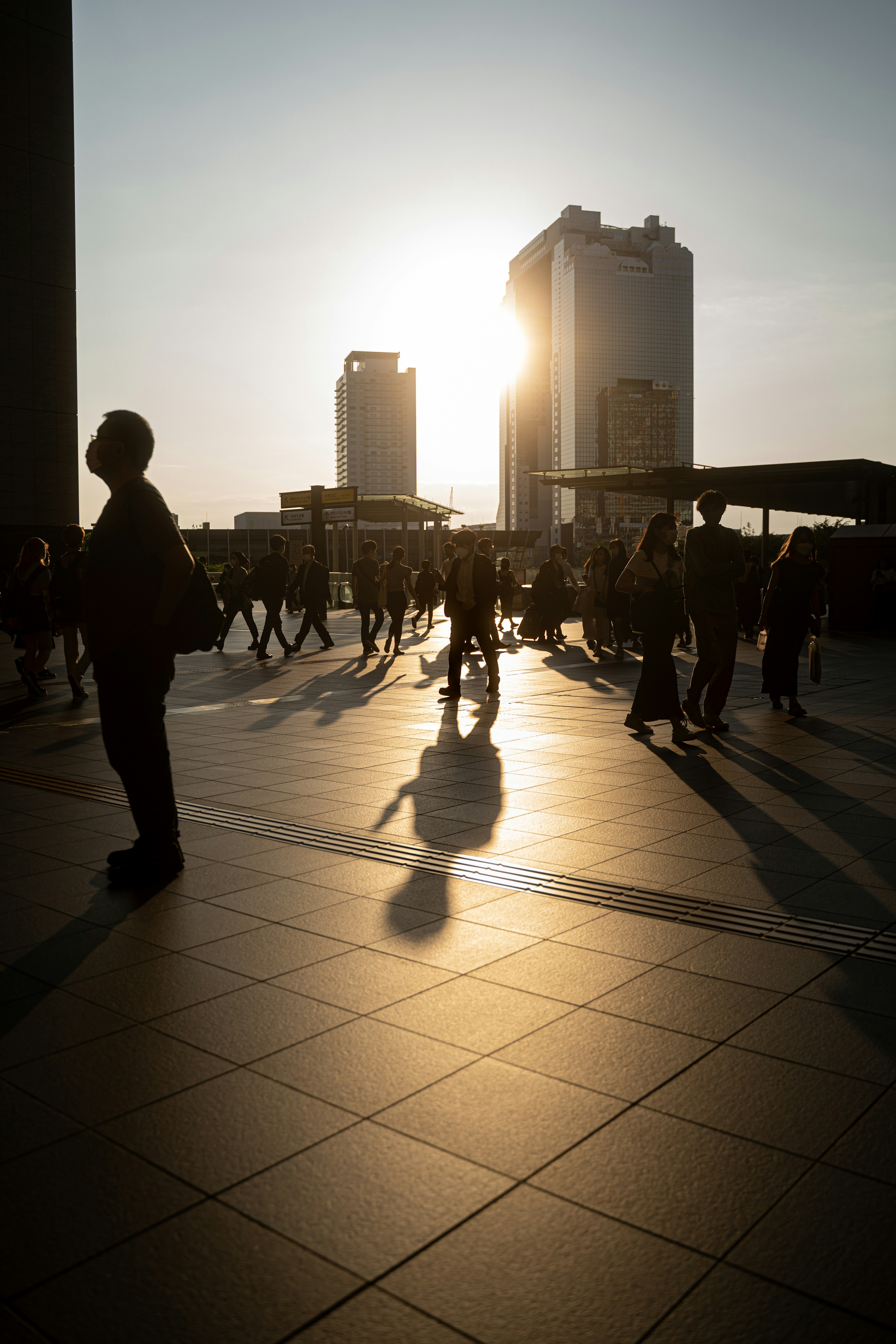 夕日をバックに人々が行き交う都会の風景