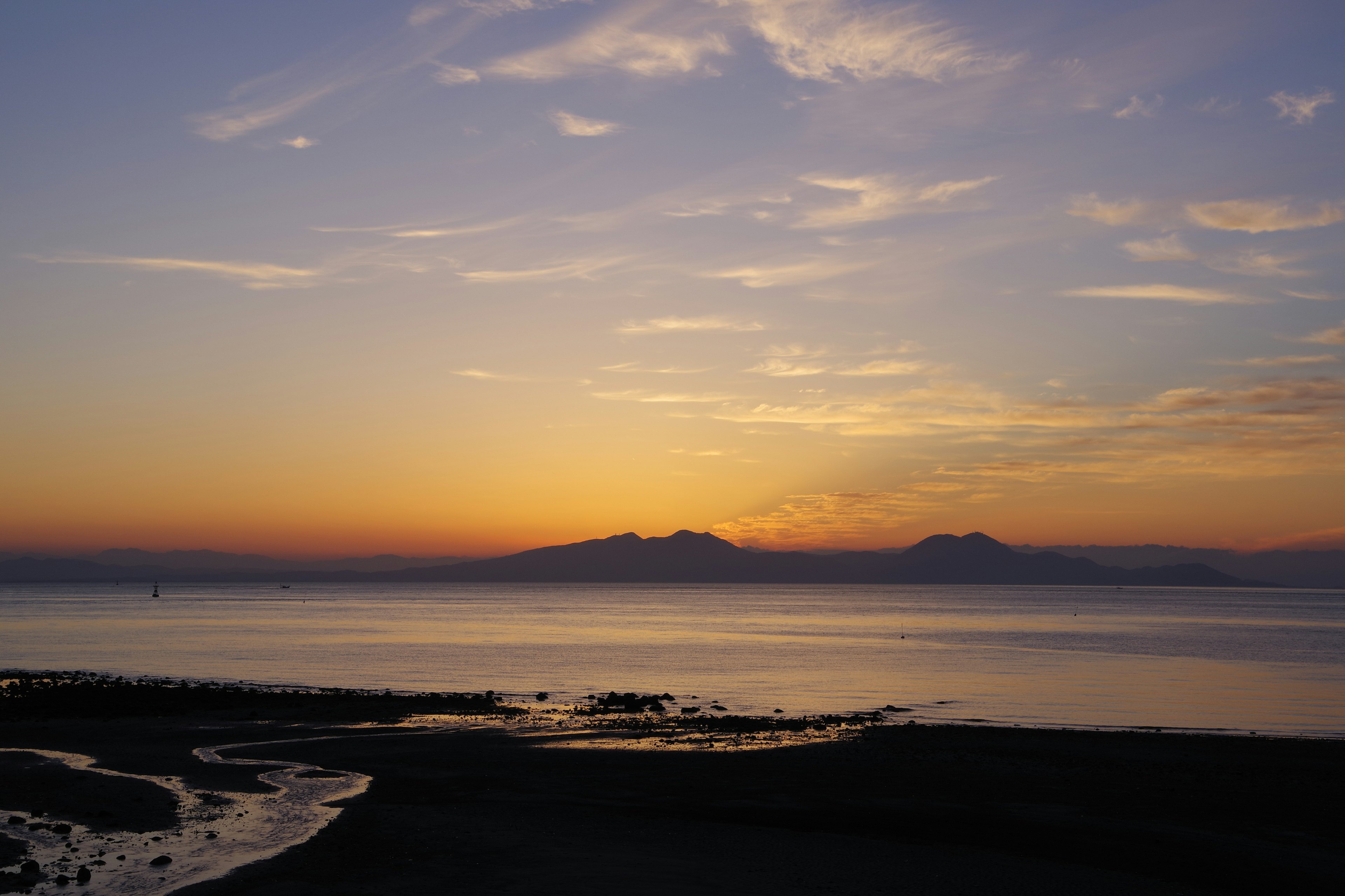 夕焼けの海と山々の風景、青とオレンジの色合い、穏やかな水面