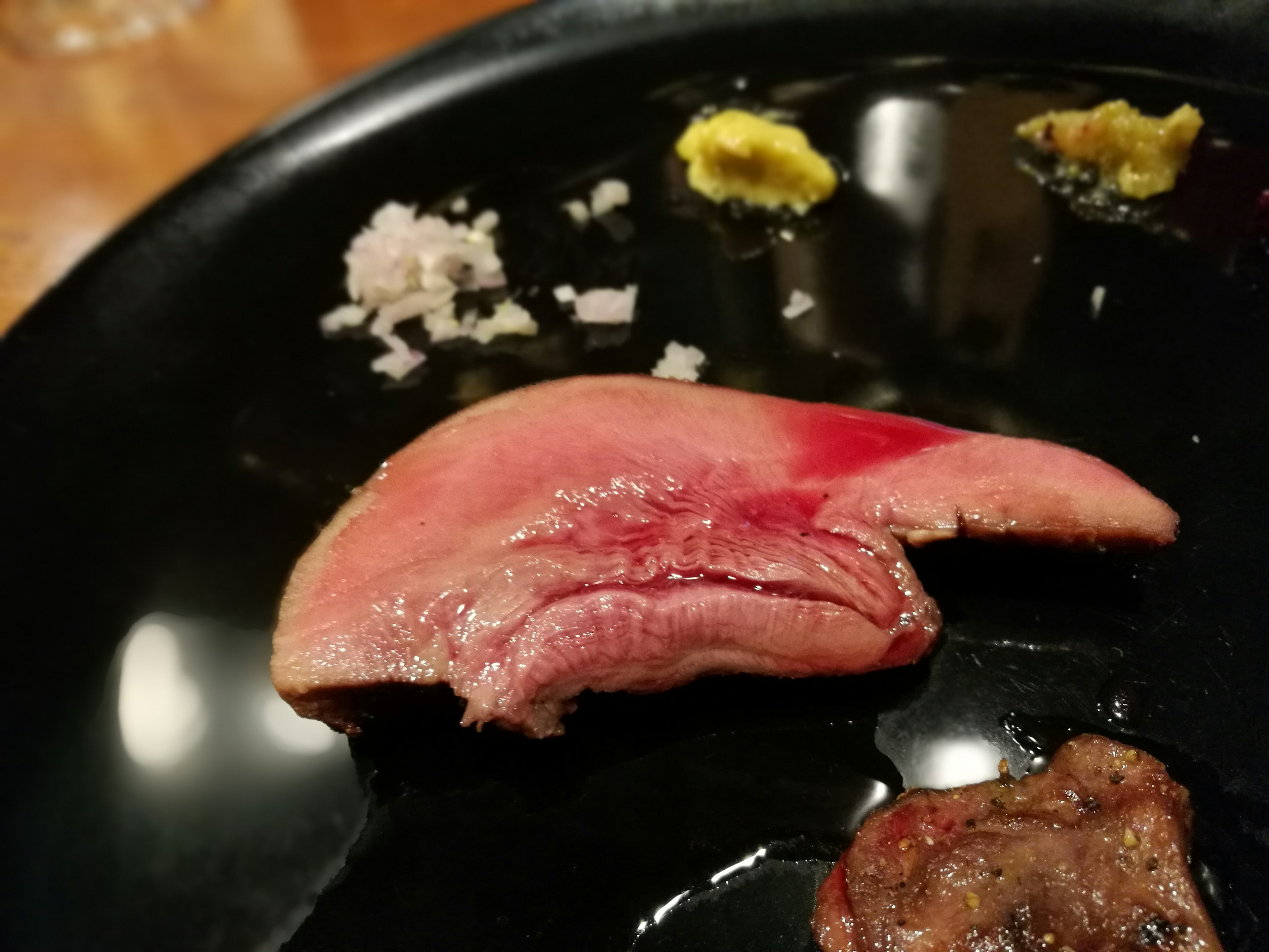 Slice of red meat on a black plate with wasabi and chopped onions