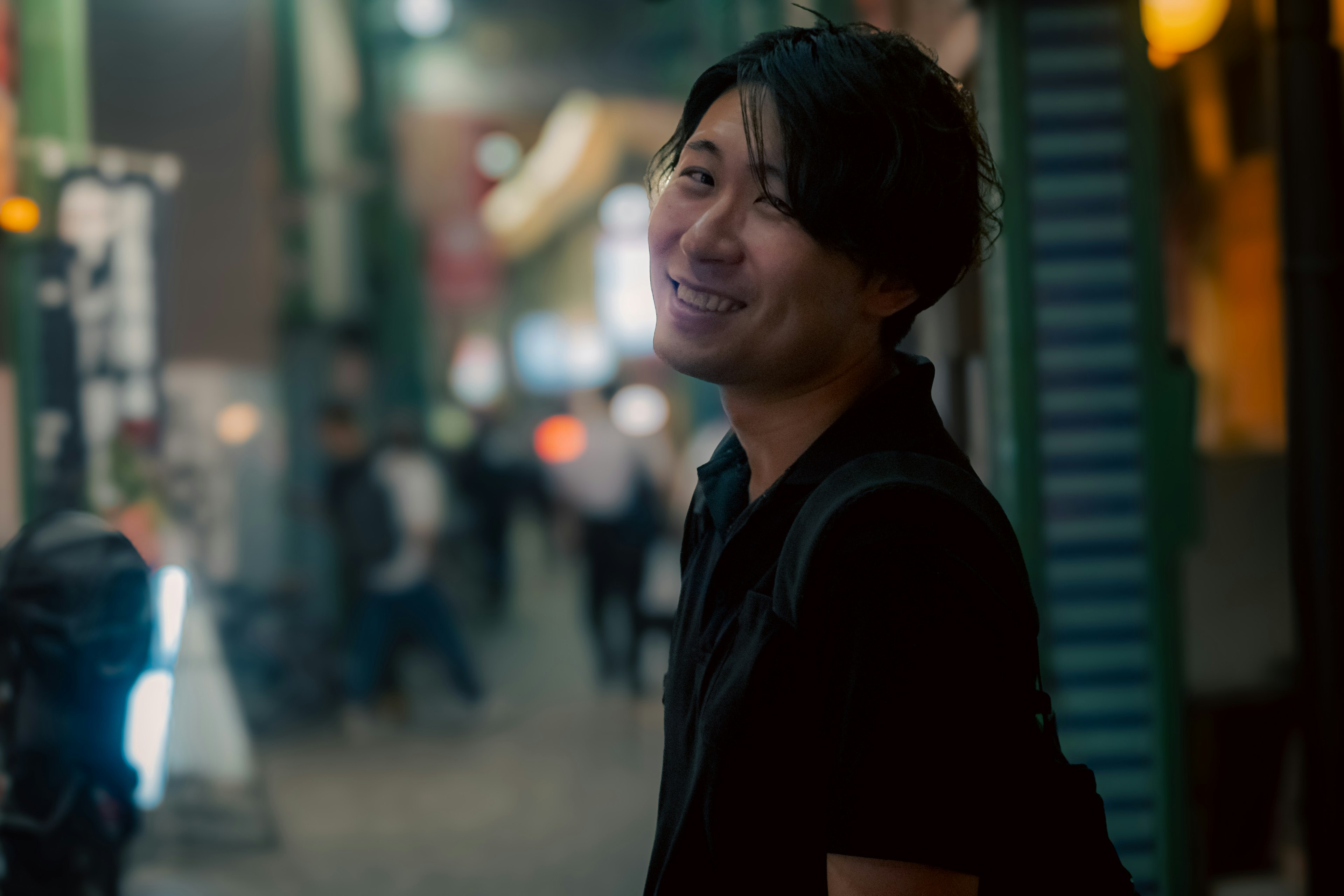 Portrait d'un homme souriant dans une rue nocturne avec des personnes floues en arrière-plan