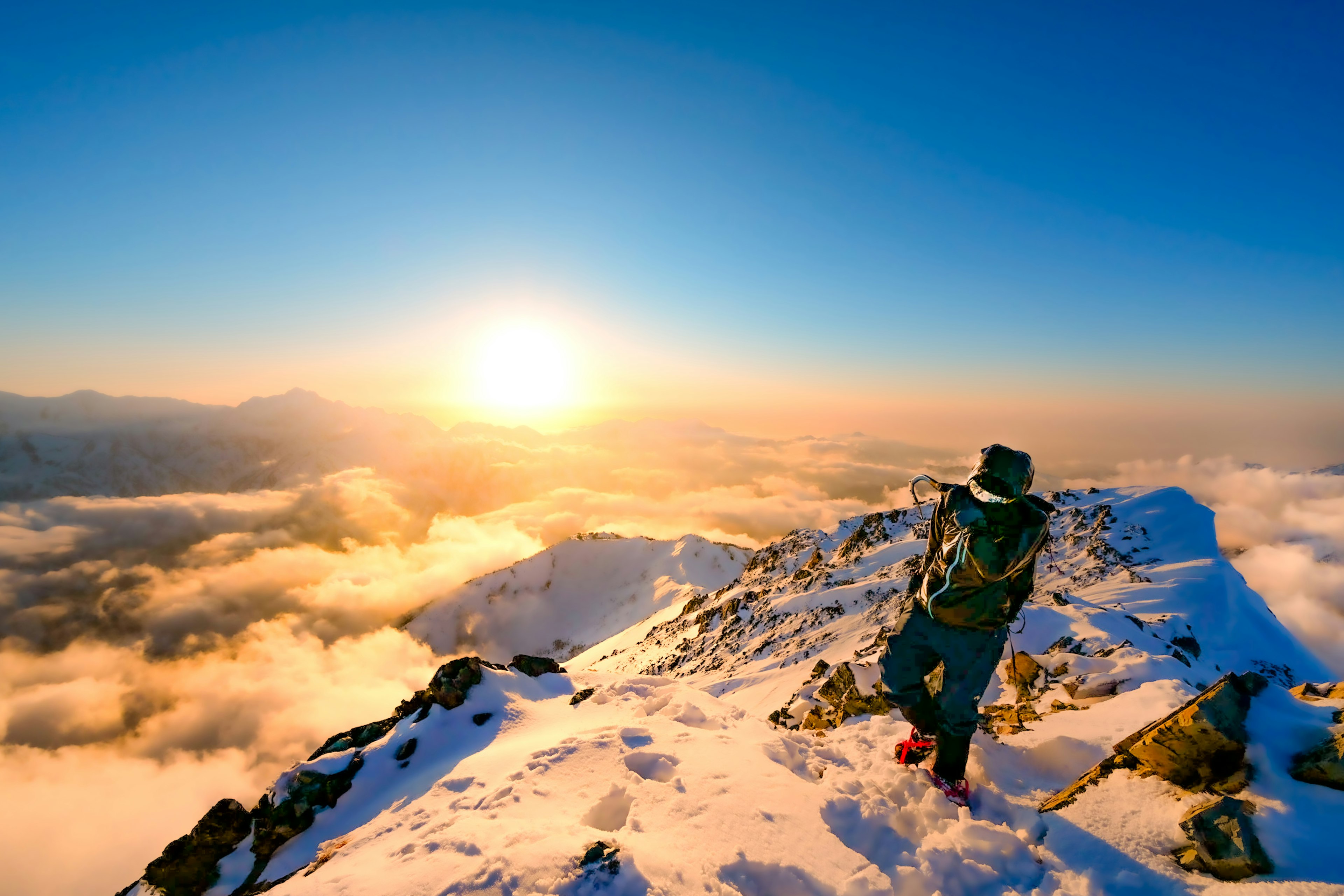 Wanderer steht auf einem schneebedeckten Berggipfel mit einem schönen Sonnenaufgang