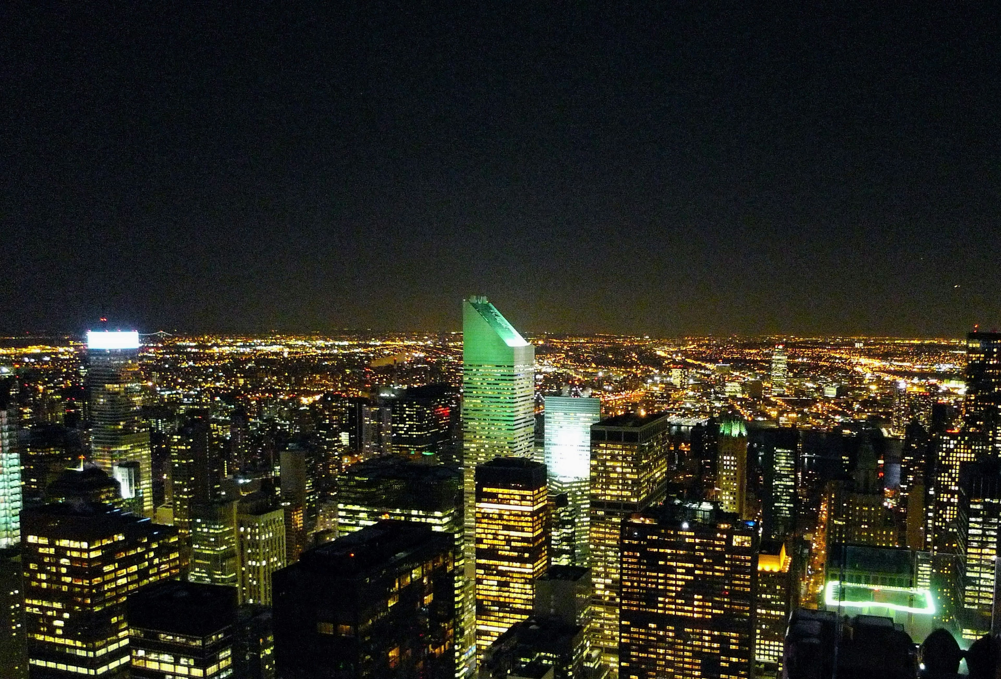 Panorama notturno della città con grattacieli e un edificio verde prominente