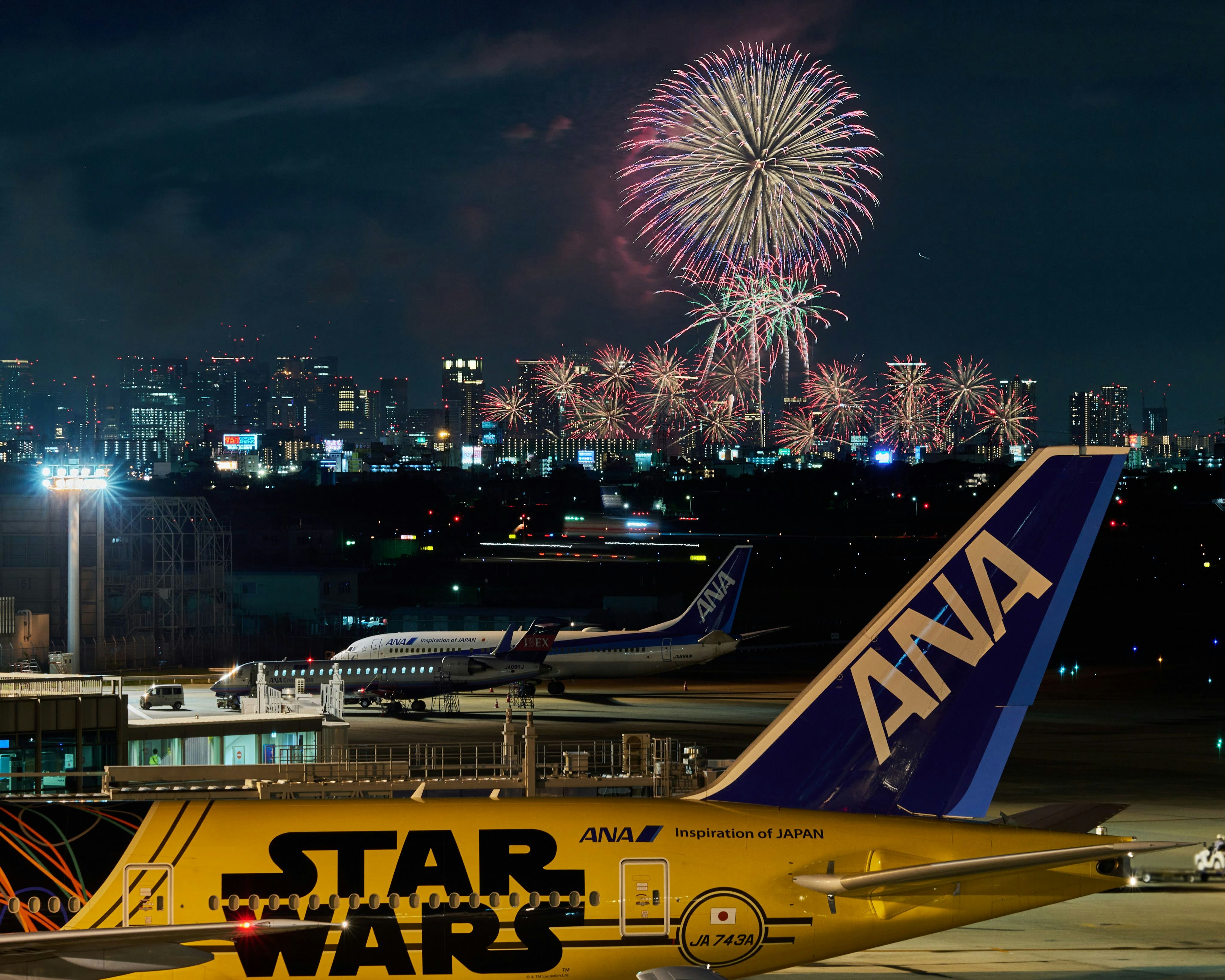 Avion ANA avec un design Star Wars au premier plan et des feux d'artifice dans le ciel nocturne