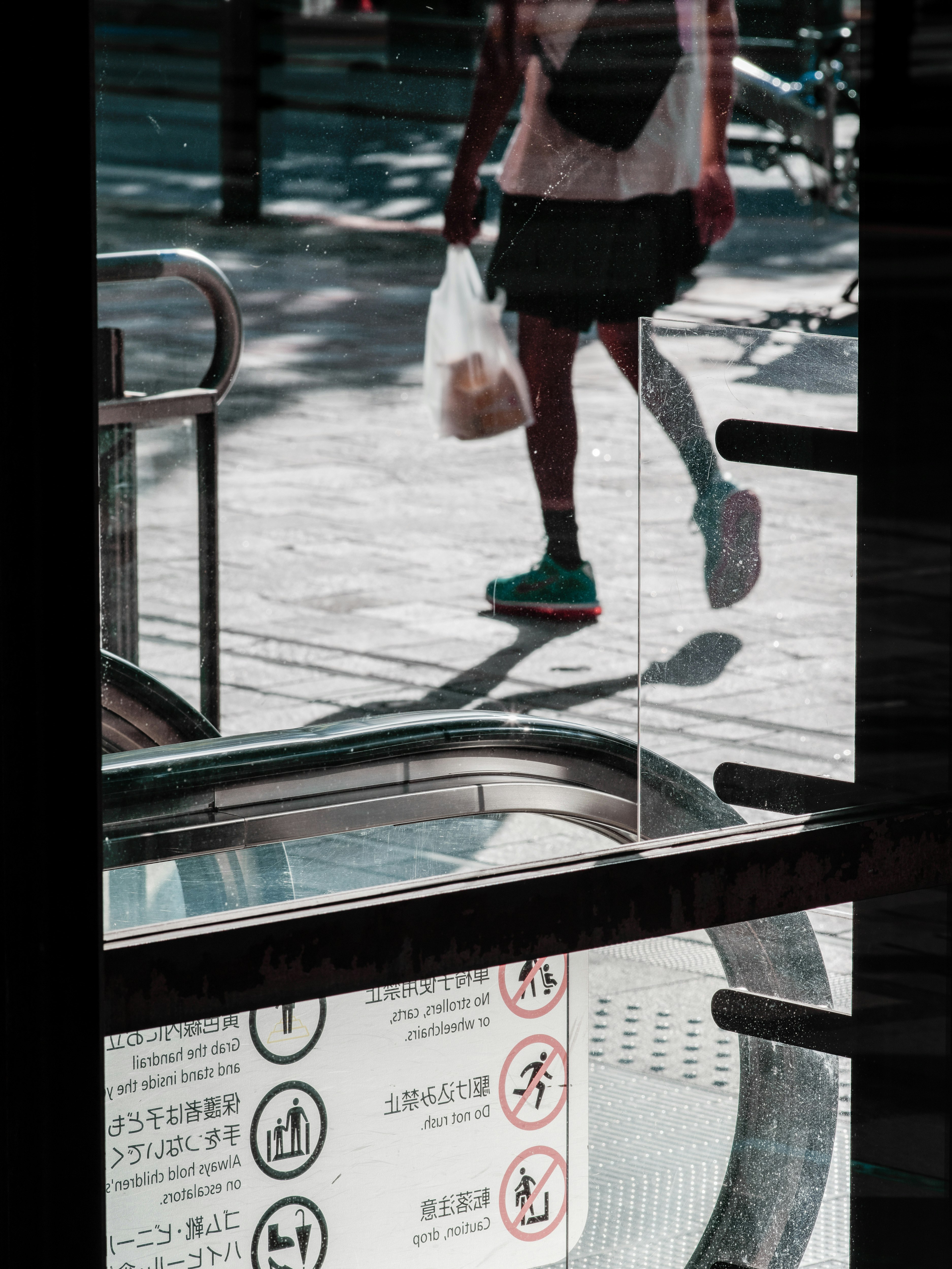 Eine Person, die vor einer Rolltreppe mit einer Tüte und sichtbaren Straßenreflexionen geht