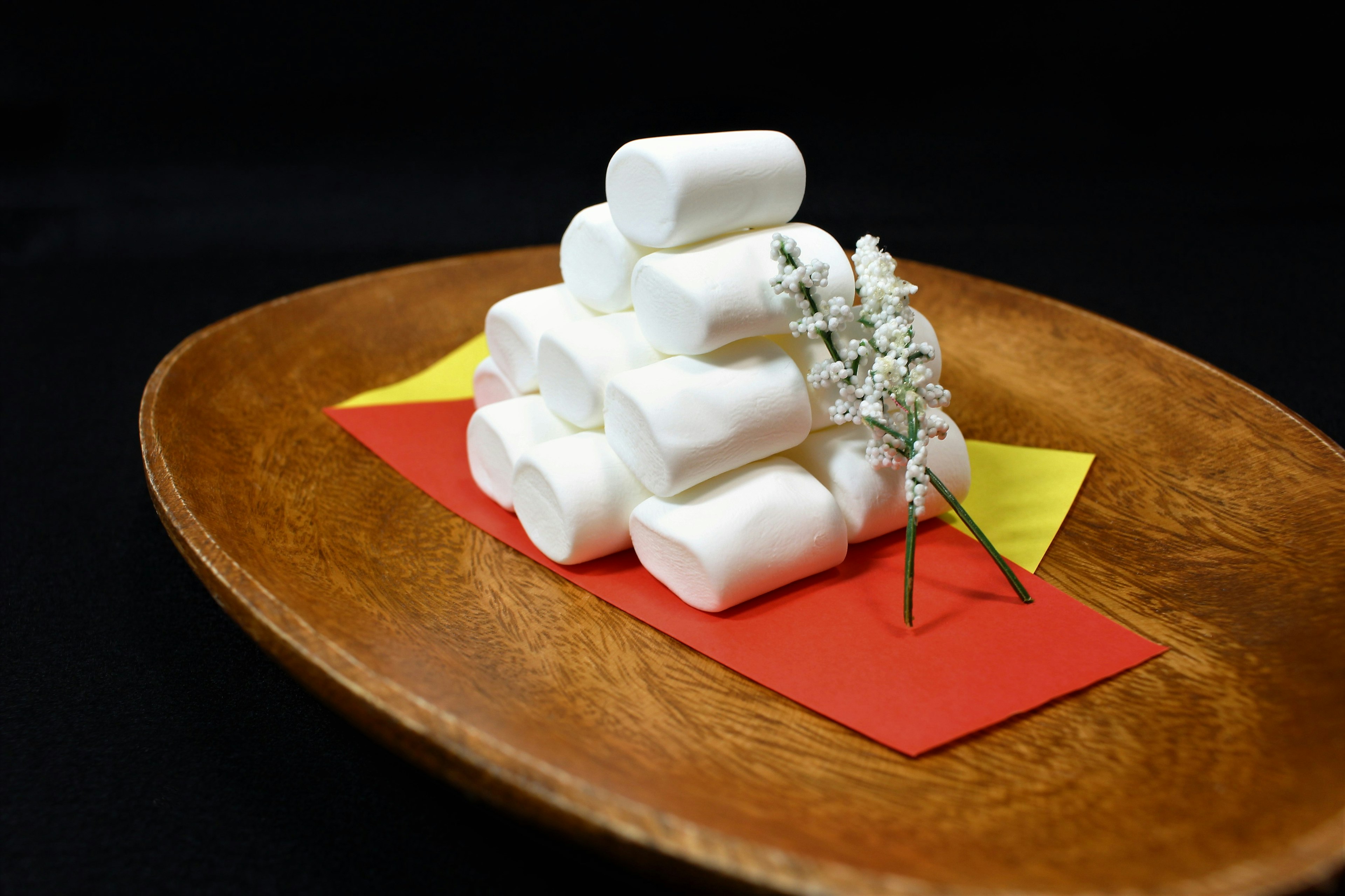 Pila di marshmallow bianchi con un fiore su un piatto di legno