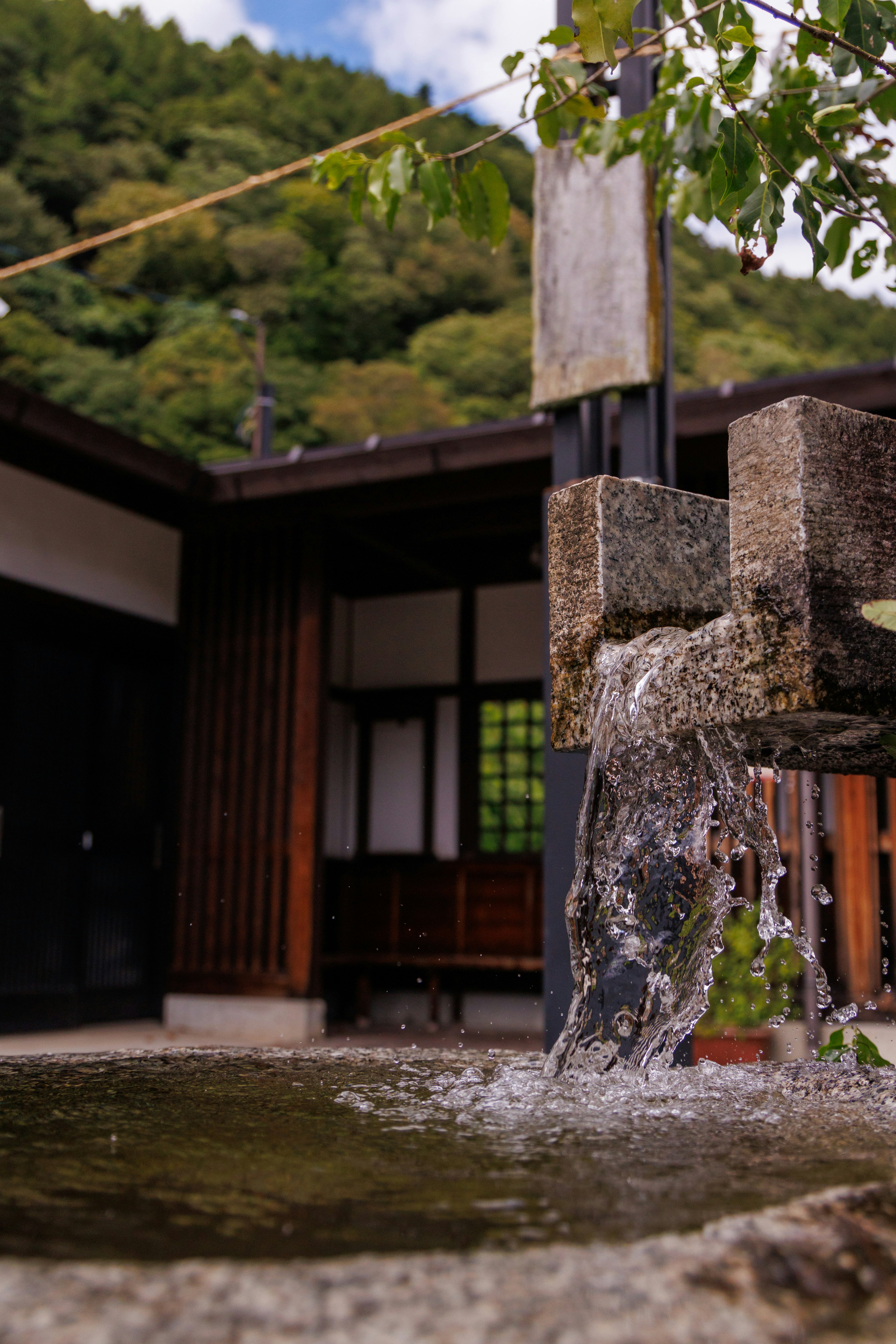 Agua fluyendo de una fuente de piedra cerca de un edificio tradicional rodeado de naturaleza