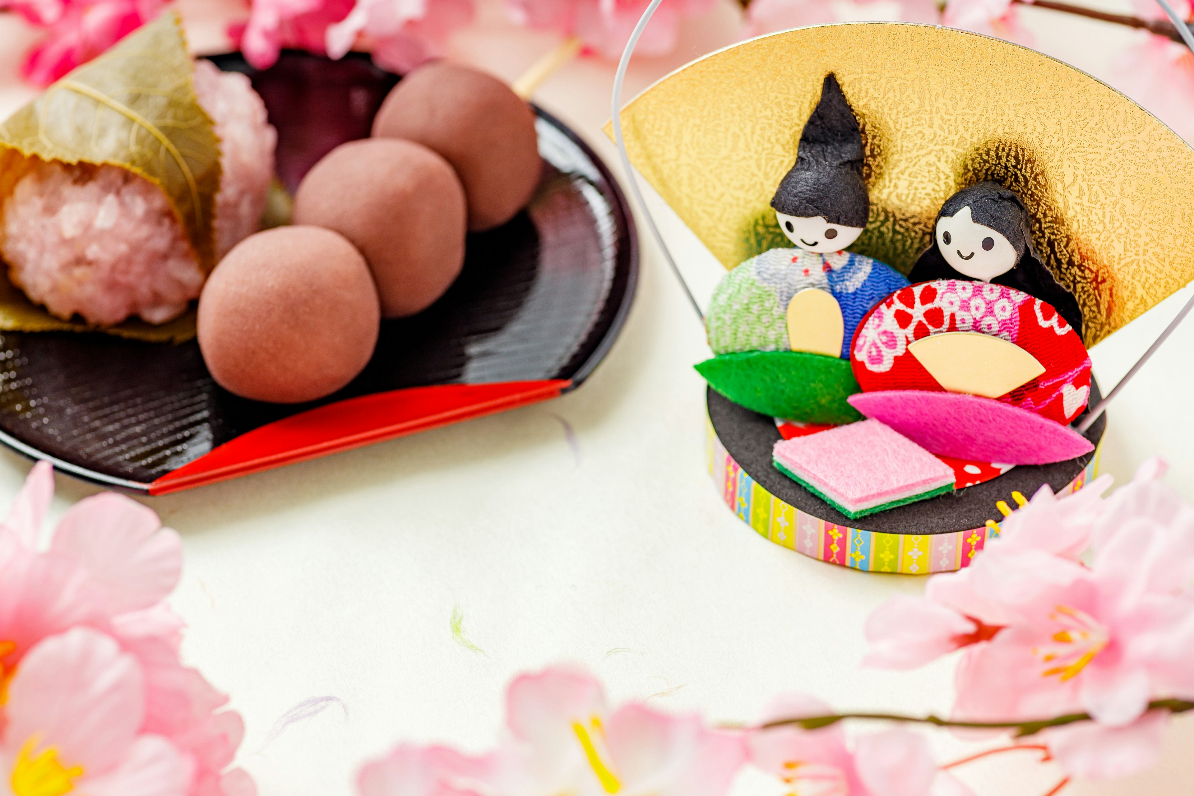 Dolci giapponesi colorati disposti con fiori di ciliegio e bambole hina