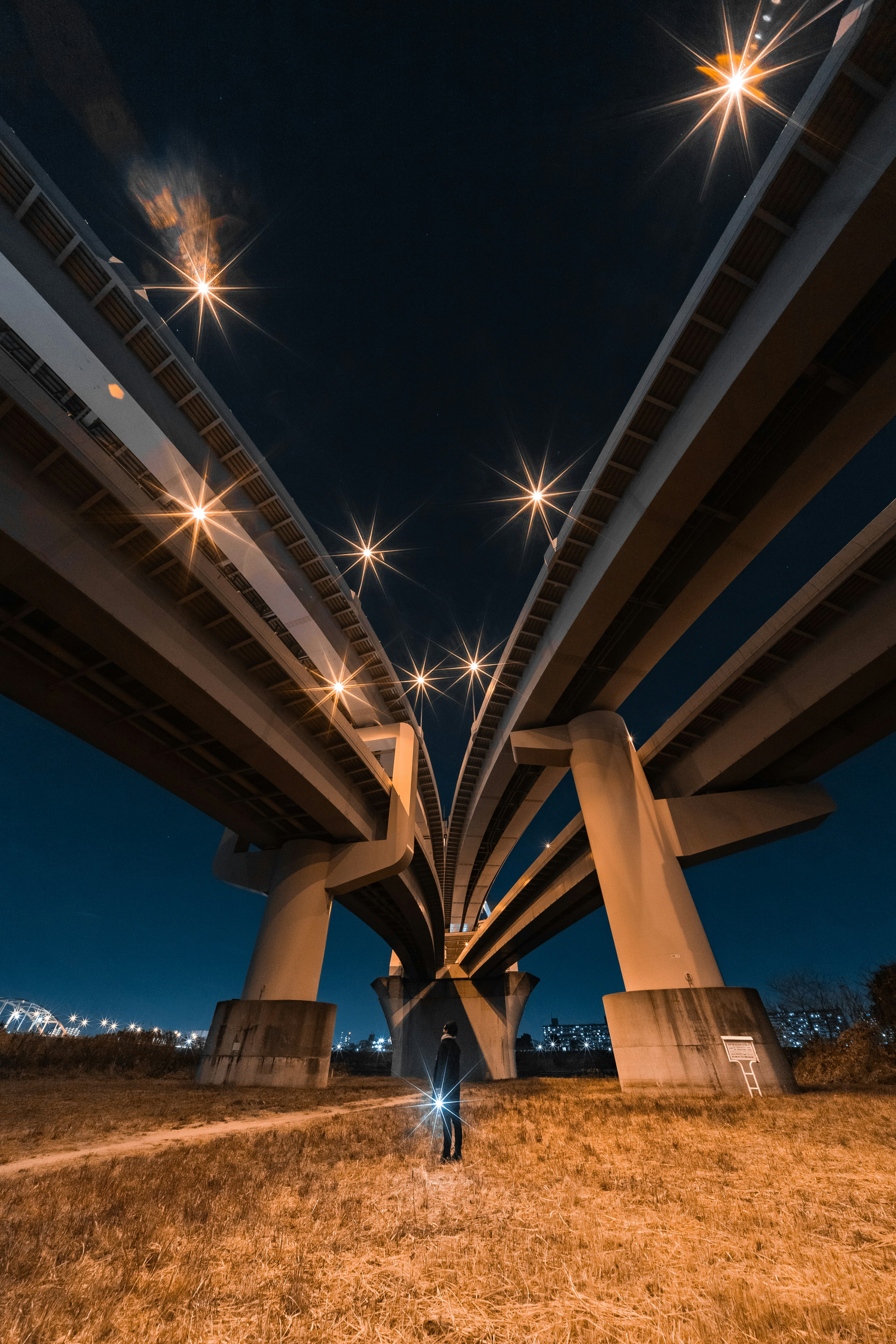 Orang berdiri di bawah jembatan layang dengan lampu jalan berkilau di malam hari