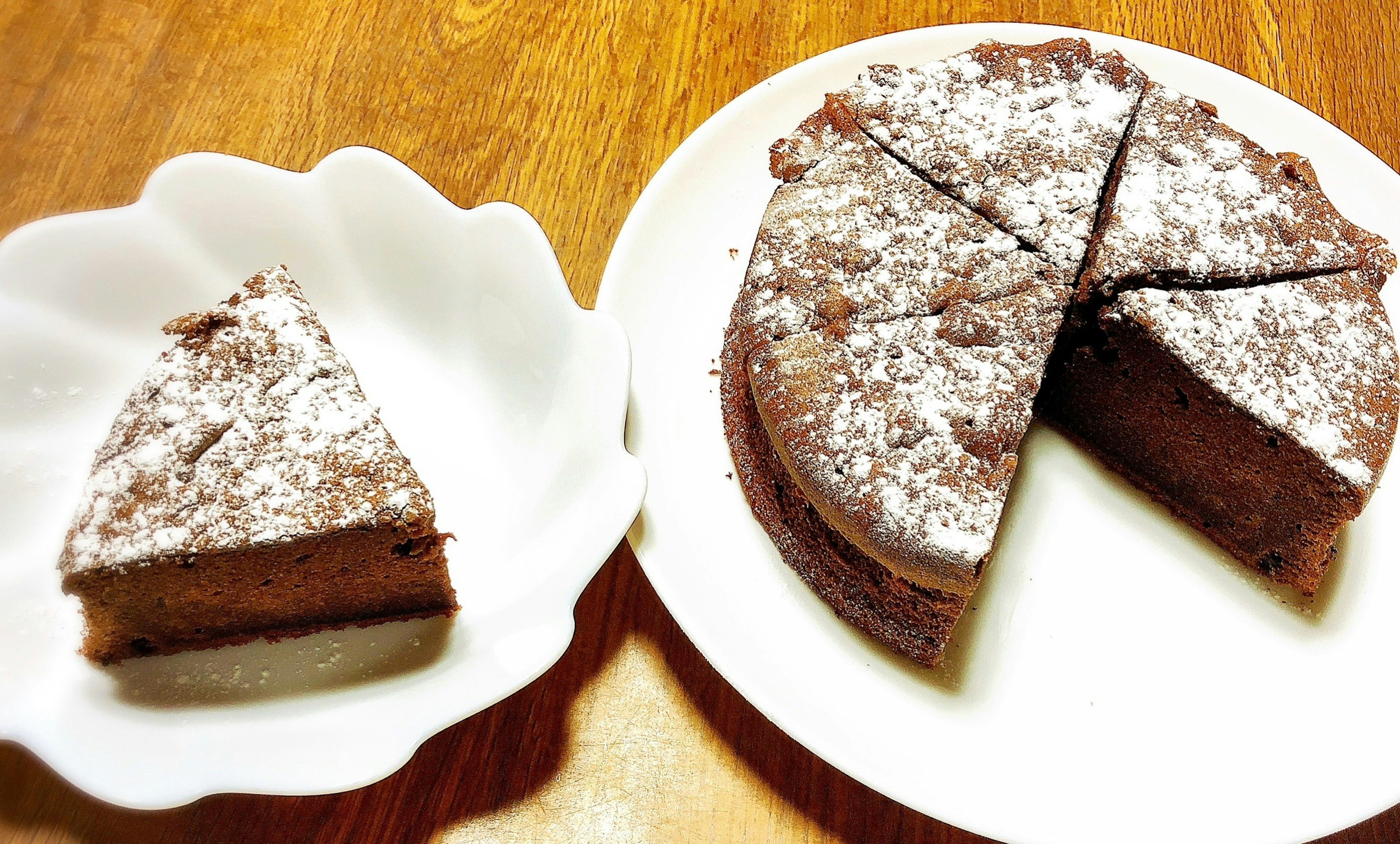 Sepotong kue coklat di atas piring putih di samping kue utuh