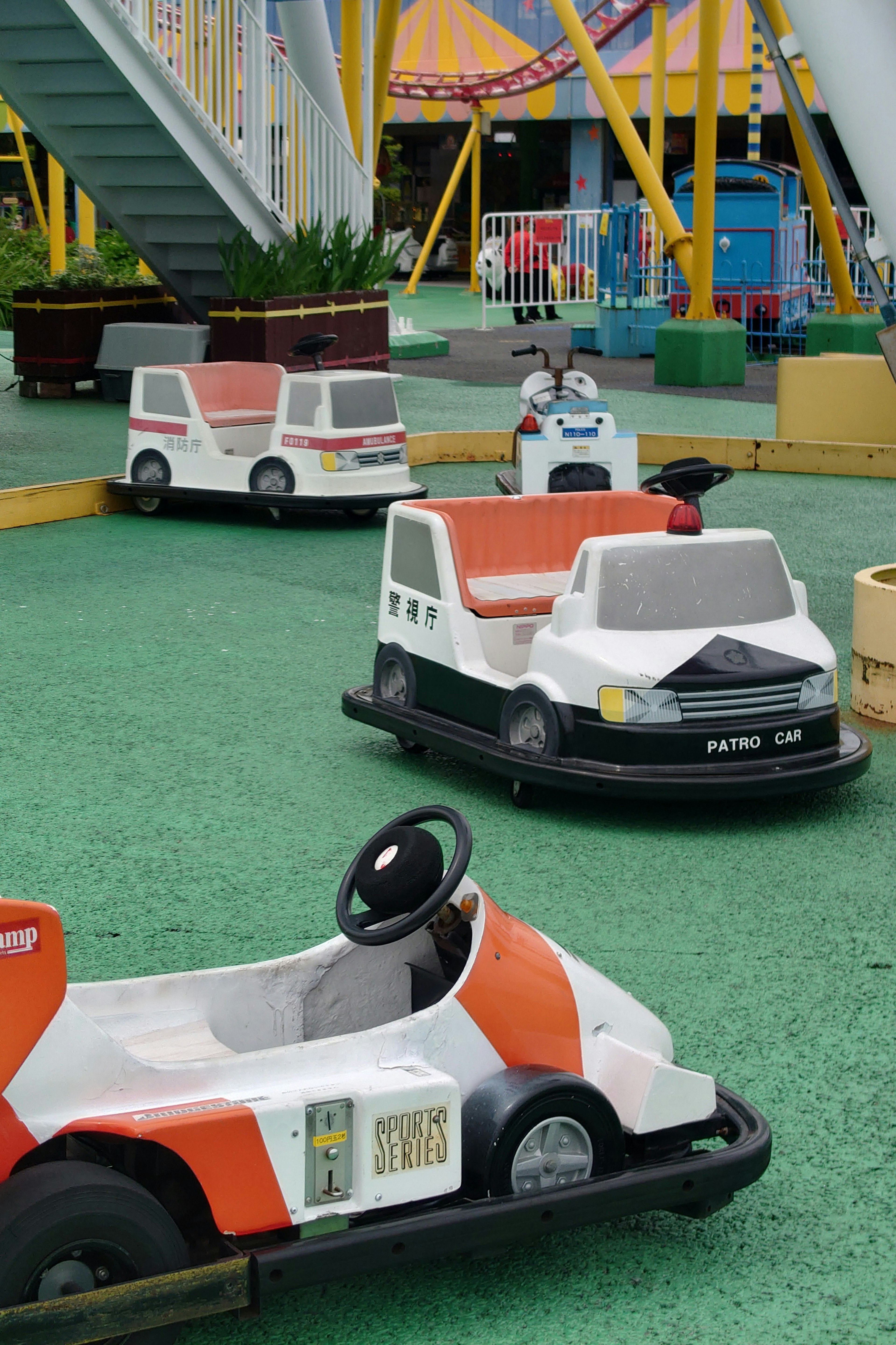 Amusement park battery cars lined up on green turf featuring white and orange vehicles