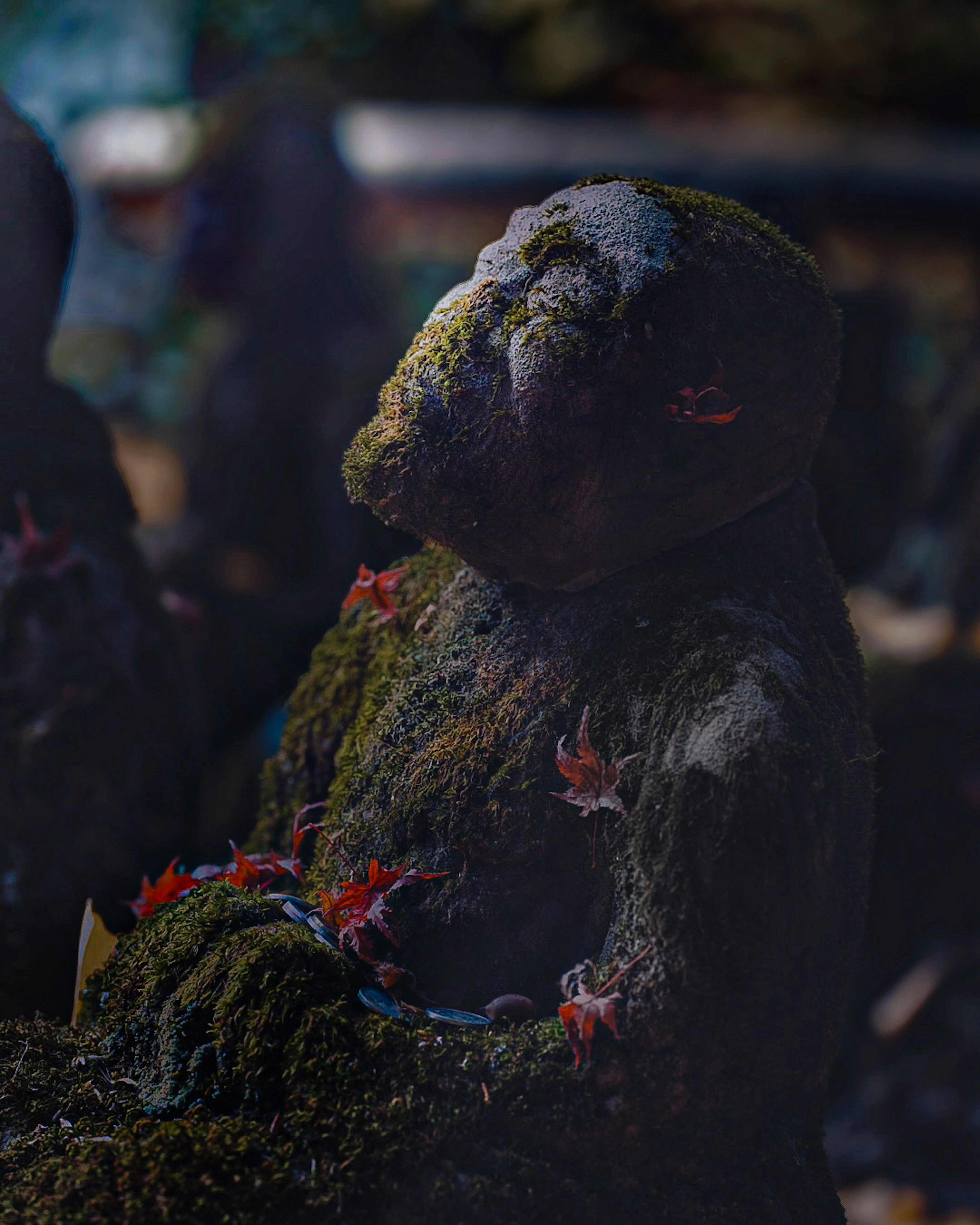 Moss-covered statue sitting quietly with fallen leaves scattered around