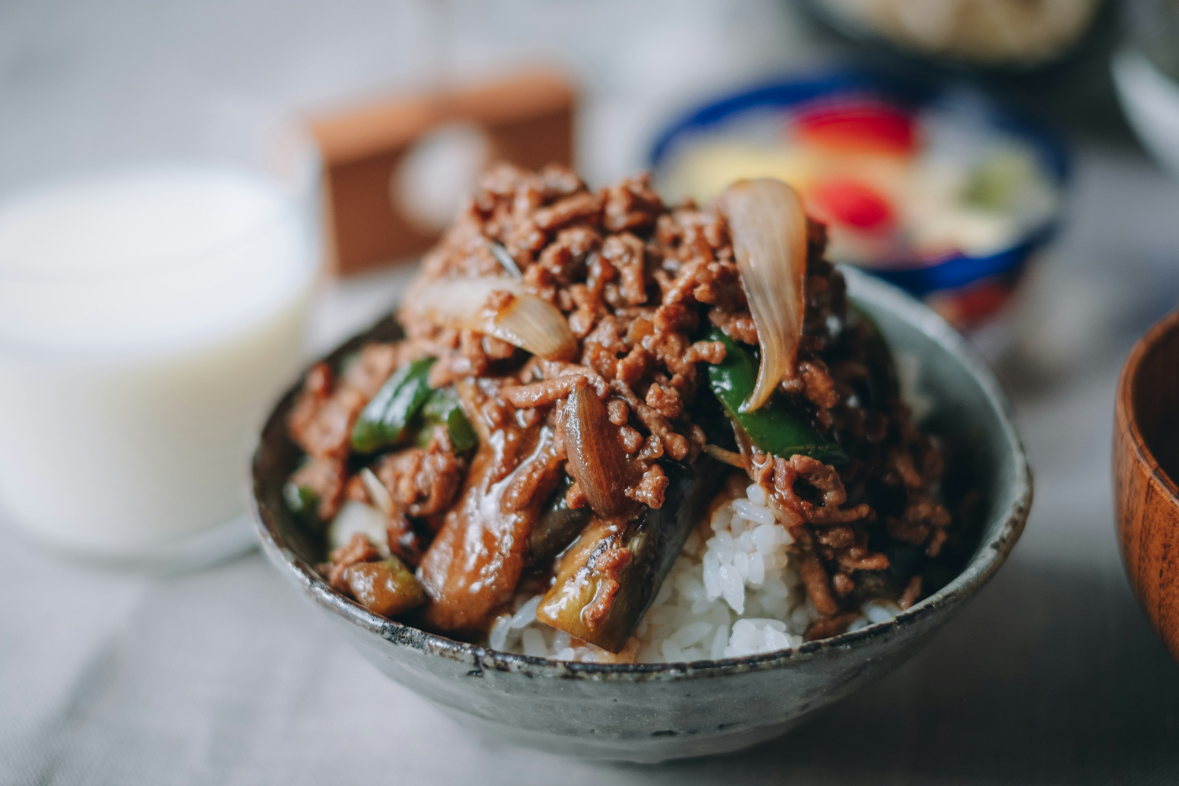 A bowl of rice topped with minced beef and vegetables alongside a beverage